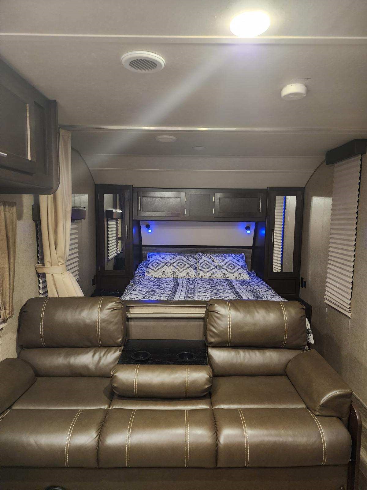 Inside an RV rental: a compact bedroom and living area with a brown leather couch, full bed, and ambient blue lighting.. Forest River Cherokee Grey Wolf 2017