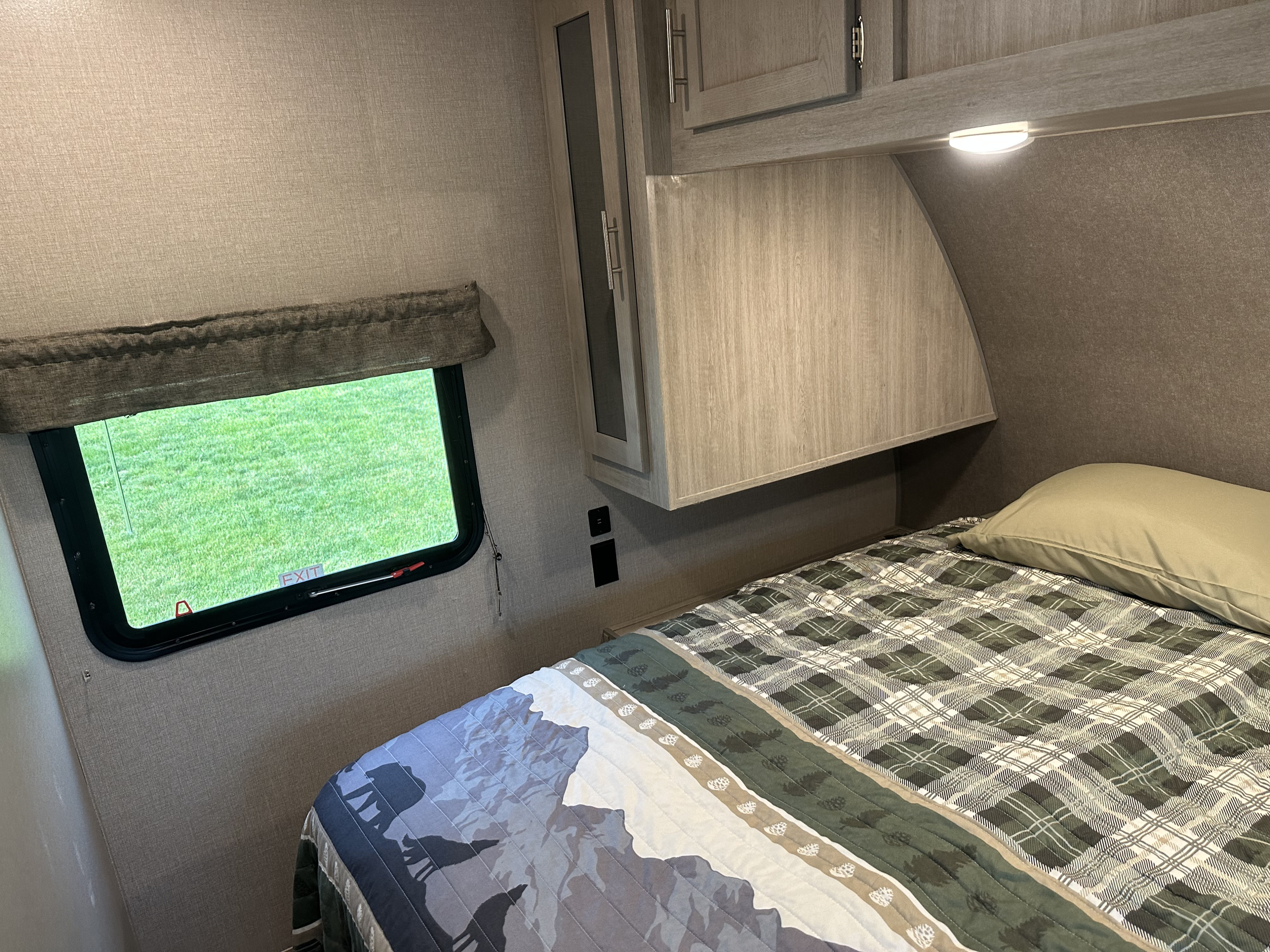 RV rental bedroom: cozy space with light wood cabinets, a window showing green grass, and nature-themed quilt.. Forest River Coachmen Catalina Legacy 2022