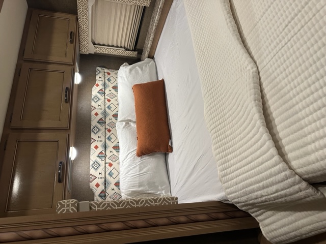 Cozy RV rental bedroom featuring a bed with white quilted bedding, an orange accent pillow, and wooden cabinets.. Thor Freedom Elite 2018