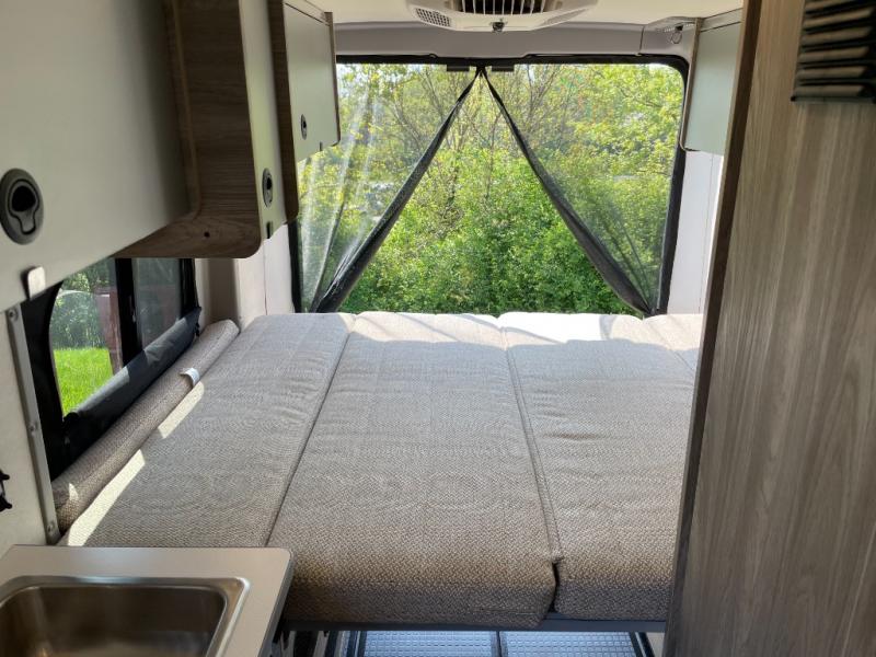 Cozy RV rental interior with a comfortable bed, rear screened window, and nature view.. Winnebago Solis 2023