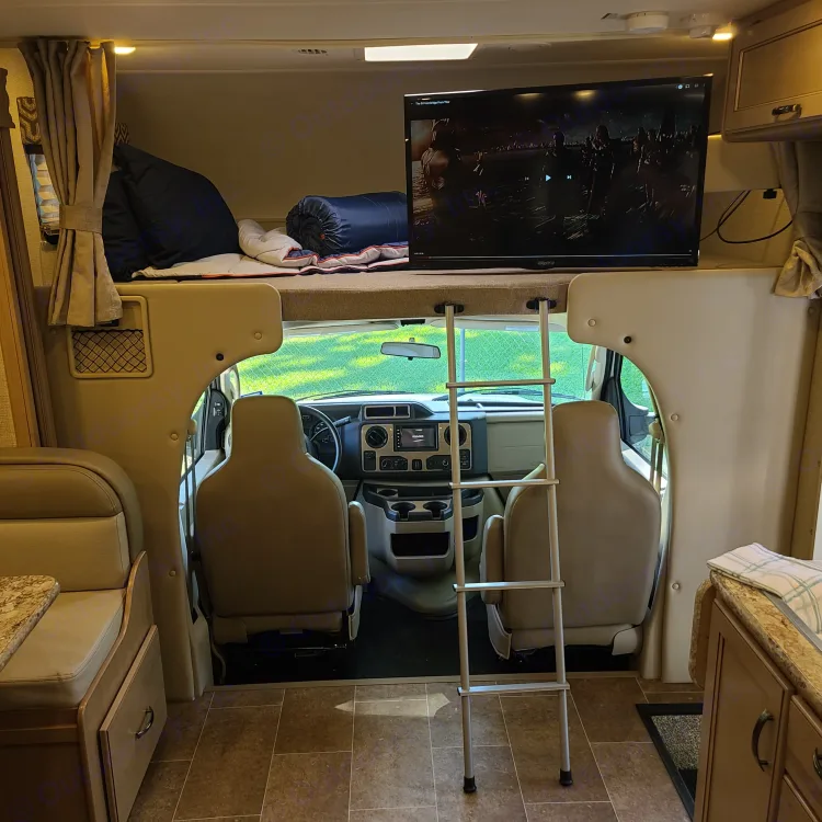 Cozy rv rental interior featuring an over-cab bed with TV, ladder, and a view into the front cab area.. Thor Motor Coach Chateau 2019