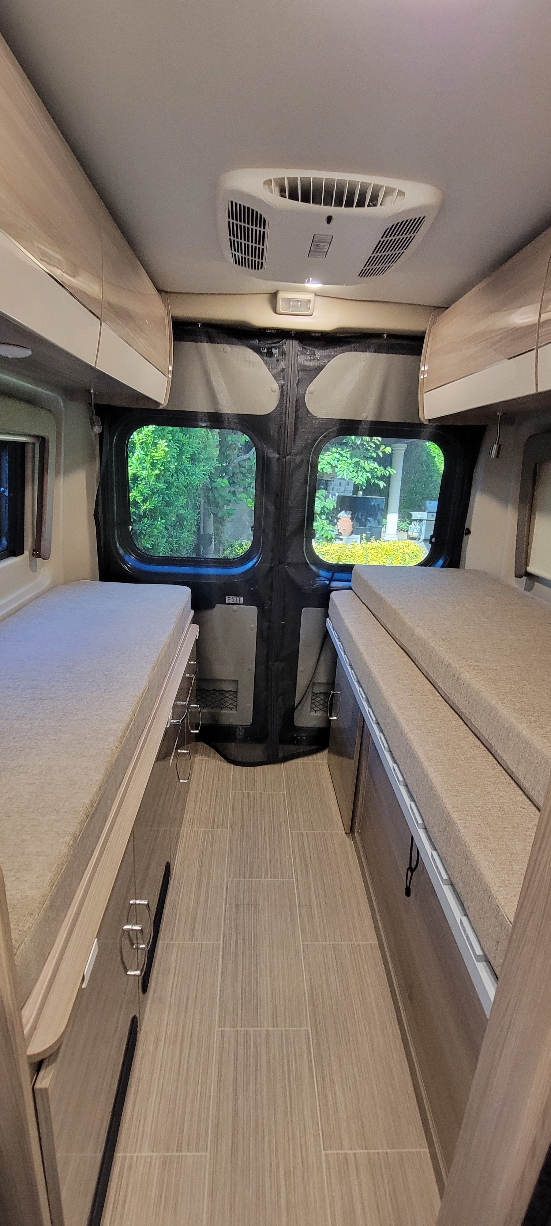 Interior of an RV rental with a narrow aisle between two beds, overhead cabinets, and a ceiling AC unit, ready for adventure.. Thor Sequence 2021