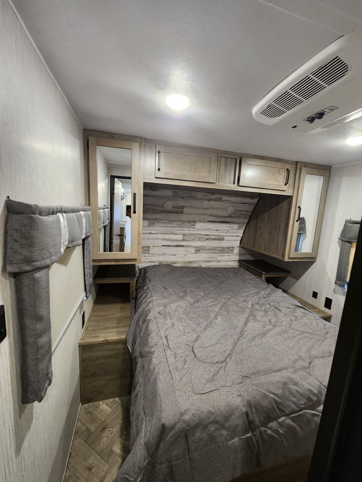 Modern RV rental bedroom featuring a comfy bed, wood accent wall, overhead cabinets, and built-in storage.. Palomino 28BHSF 2022