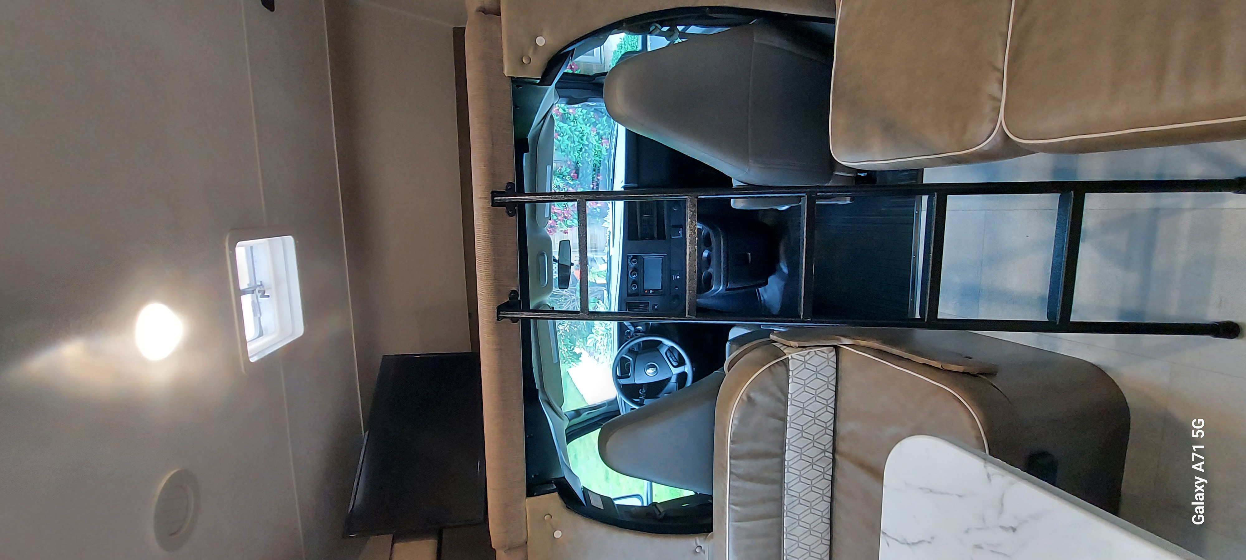 RV rental interior view: the front cab and driver's area are visible, along with a ladder leading to the overhead bunk bed.. Forest River Coachmen Freelander 2021
