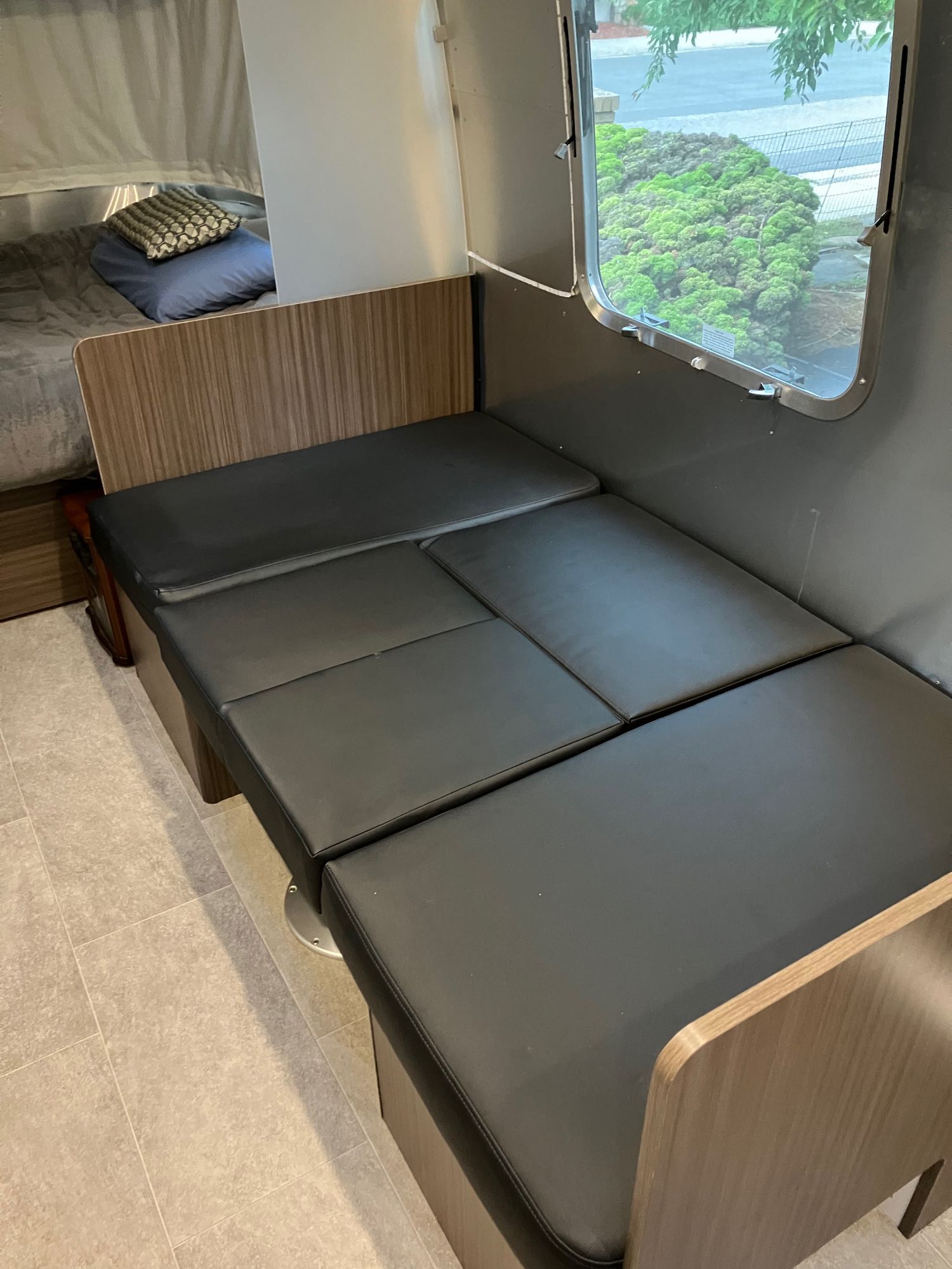 Cozy RV rental interior: black cushioned dinette converts to a bed, beside a sleeping area with pillows and a window.. Airstream Caravel 2022