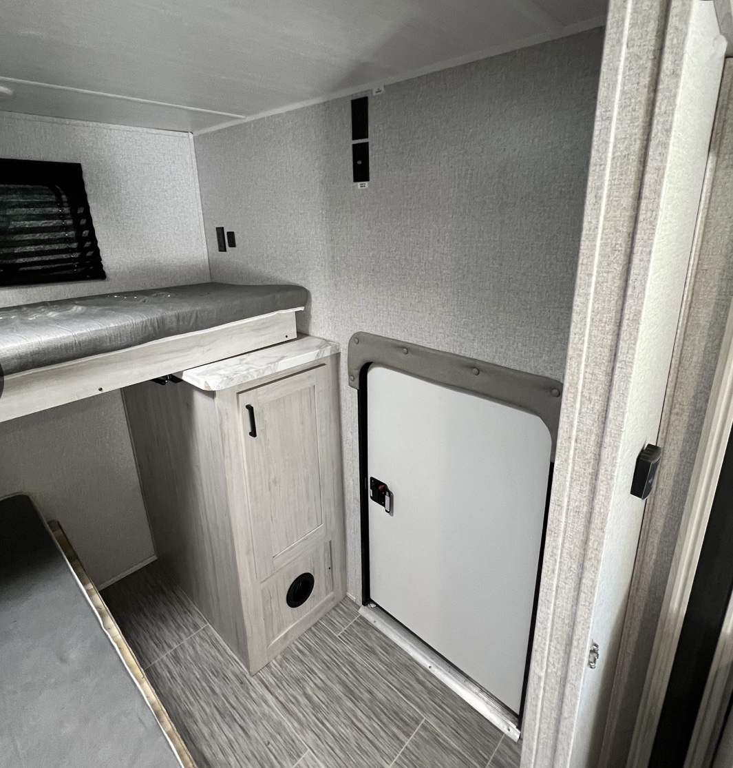 RV rental interior: bunk bed with grey mattress, cabinet, and large storage access door. Functional space for your RV rental journey.. East to West Silver Lake 2022