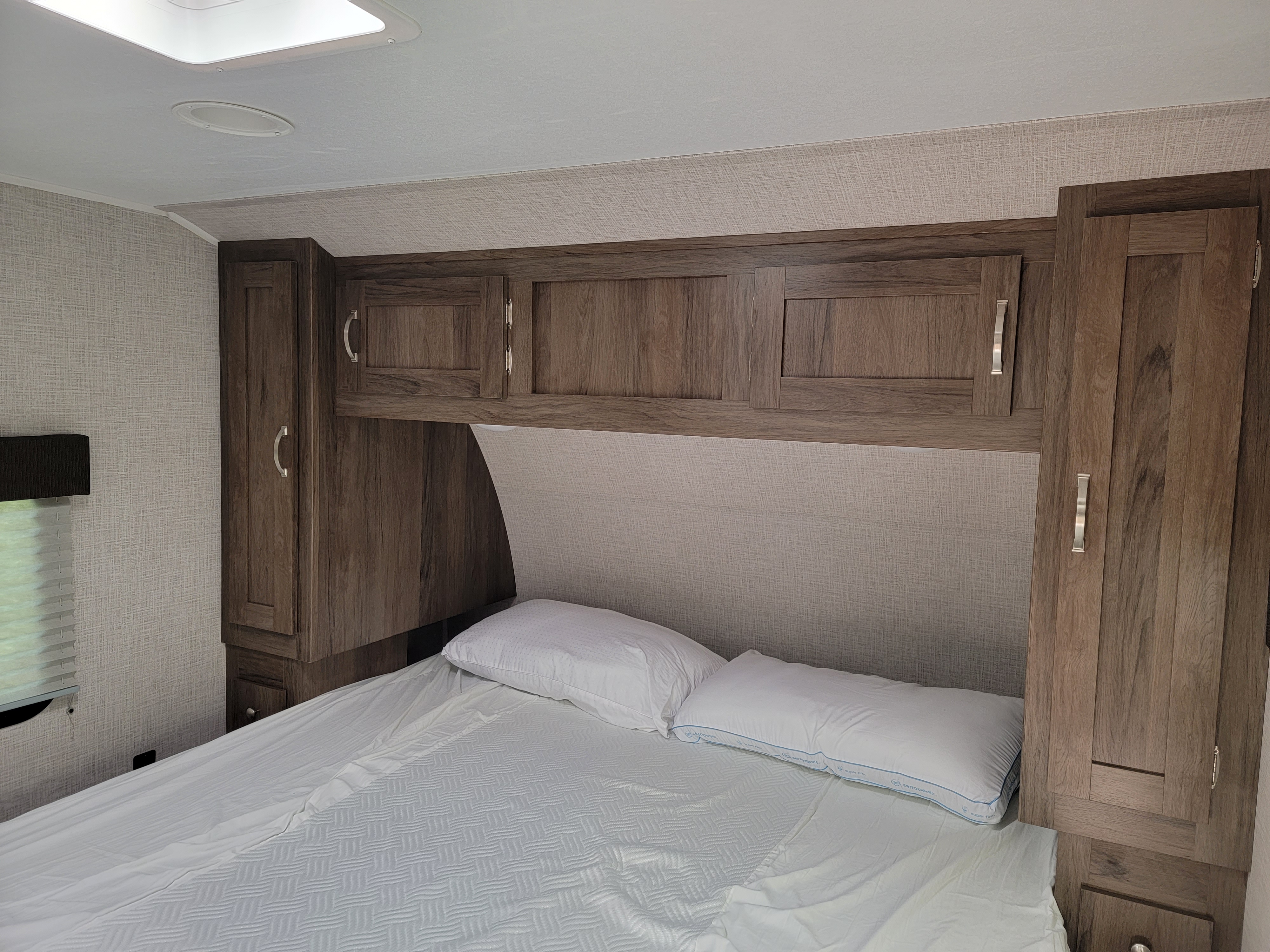 Cozy RV rental bedroom with a comfy bed, textured headboard, and ample wooden storage cabinets.. East to West Della Terra 2021
