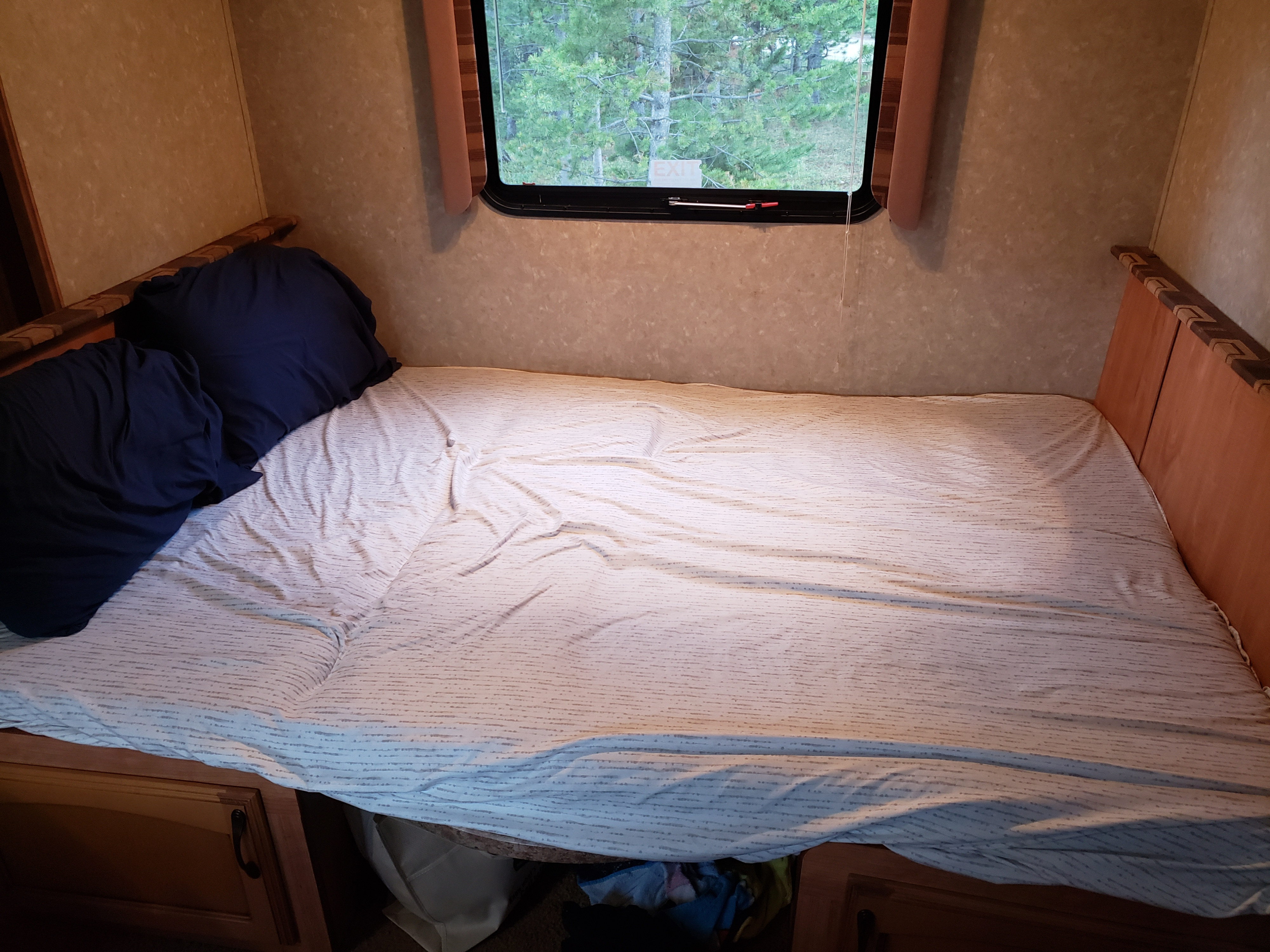 This RV rental offers a cozy sleeping area: a bed with pillows, under-bed storage, & a window view of trees.. Gulf Stream Ameri-Lite 2011