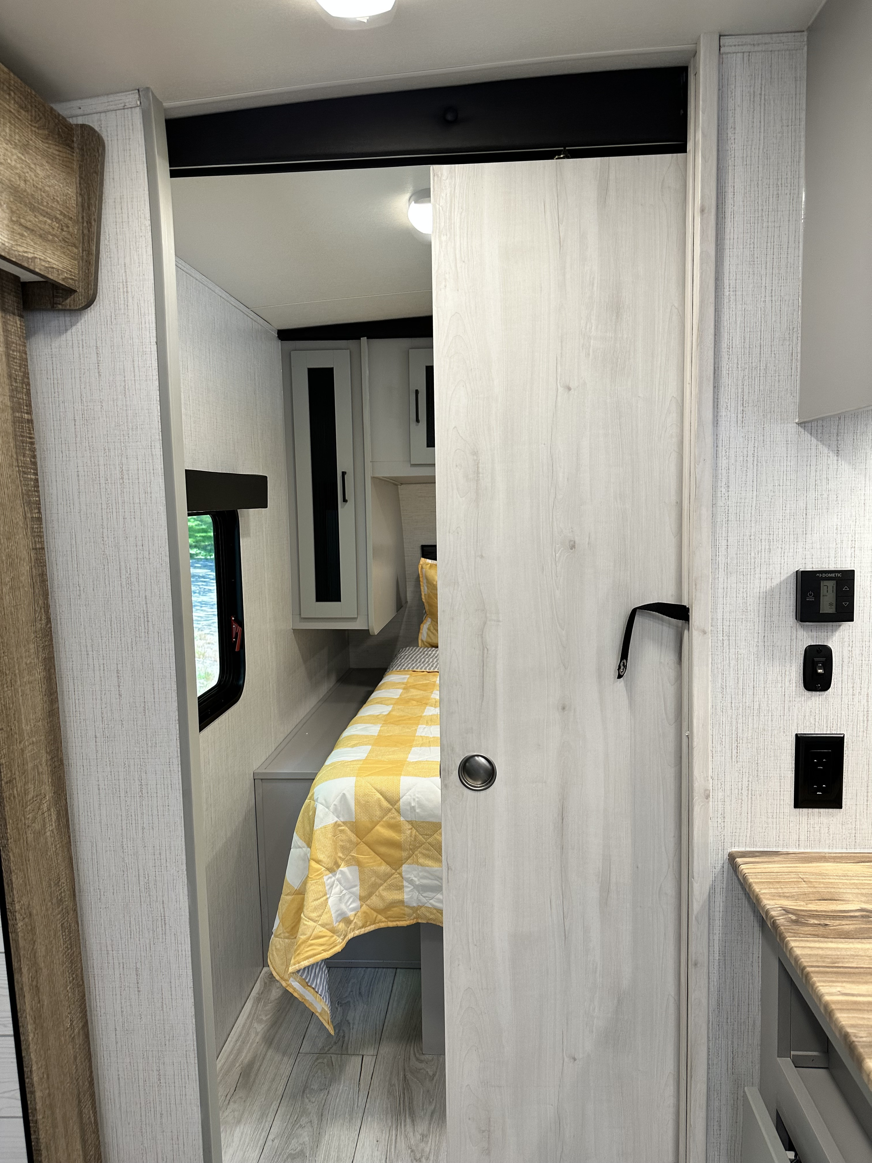 Modern RV rental interior: A bright bedroom with a yellow quilt, seen through an open sliding door. Dometic thermostat visible.. Heartland RVs North Trail 2022