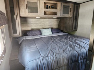 Inside your comfy RV rental: A large bed with a soft comforter, throw pillows, and built-in overhead storage for travel gear.. Heartland RVs North Trail 2021
