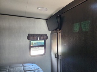 Inside an RV rental: a comfortable bedroom featuring a window, wall-mounted TV, and built-in wardrobe.. Heartland RVs North Trail 2021