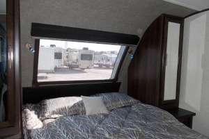 Cozy RV bedroom for your RV rental, featuring a large window with views of other units, offering comfort for travel.. Jayco White Hawk 2018
