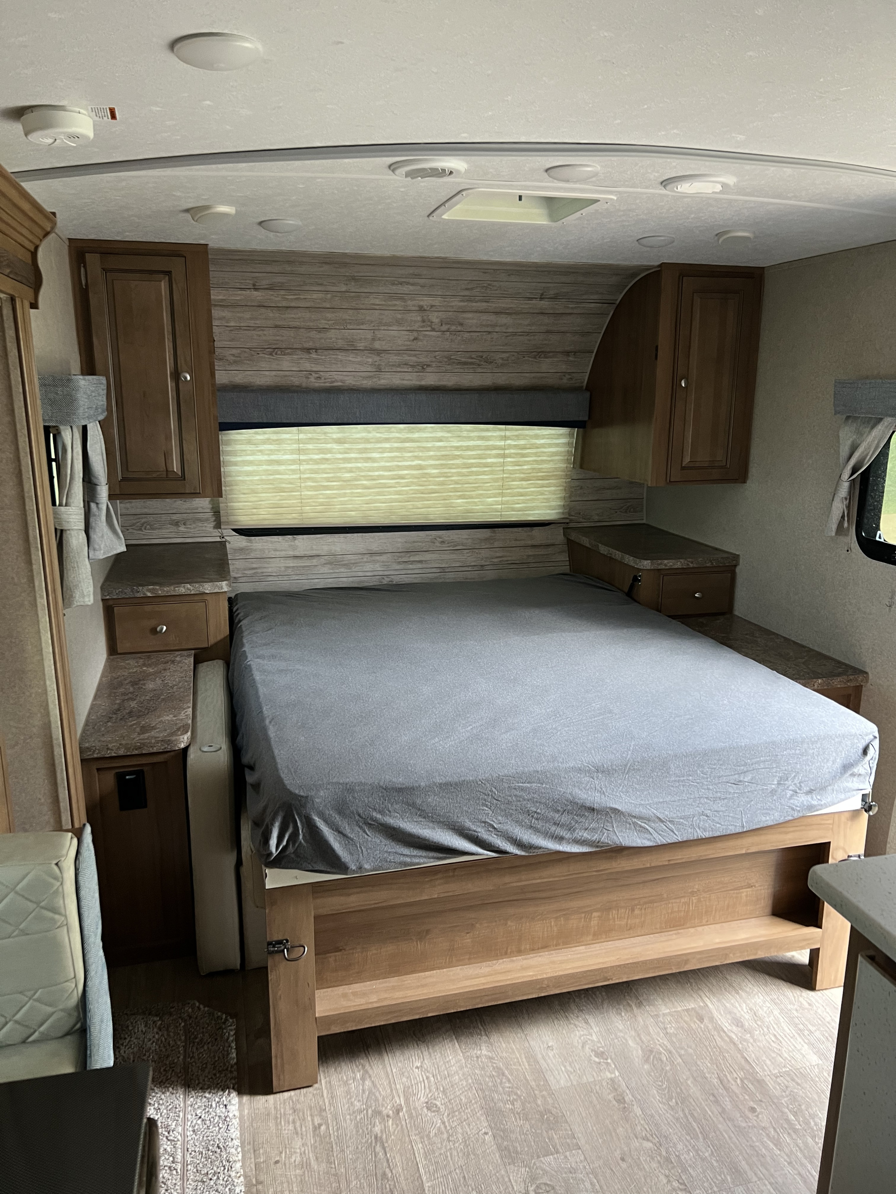 Spacious RV rental bedroom with a grey-sheeted bed, side cabinets, and window, offering a comfortable stay.. Forest River Rockwood Mini Lite 2019