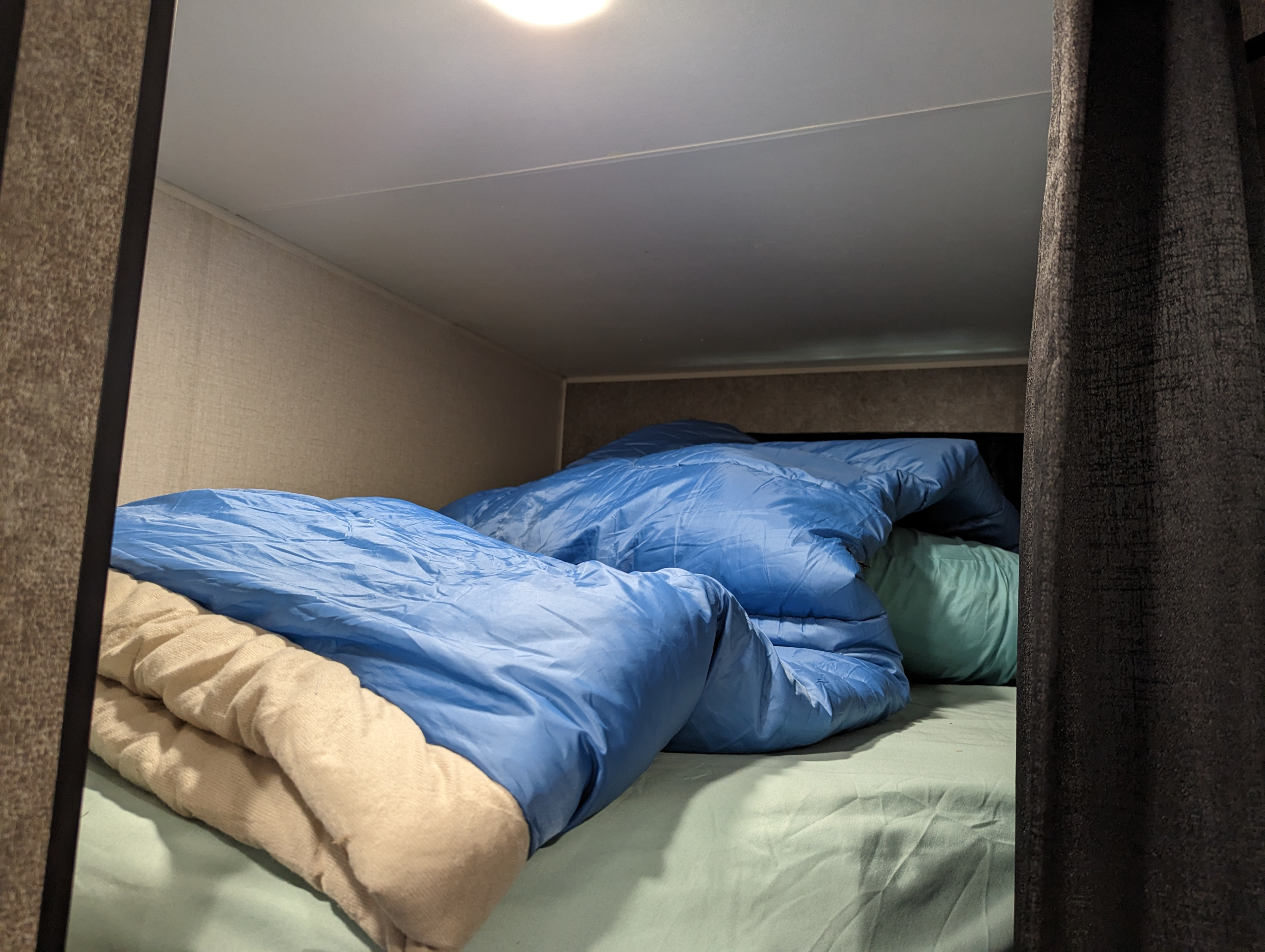 Inside an rv rental: a cozy bunk bed with blue sleeping bags, light green sheets, and a beige blanket.. Starcraft Autumn Ridge 2021