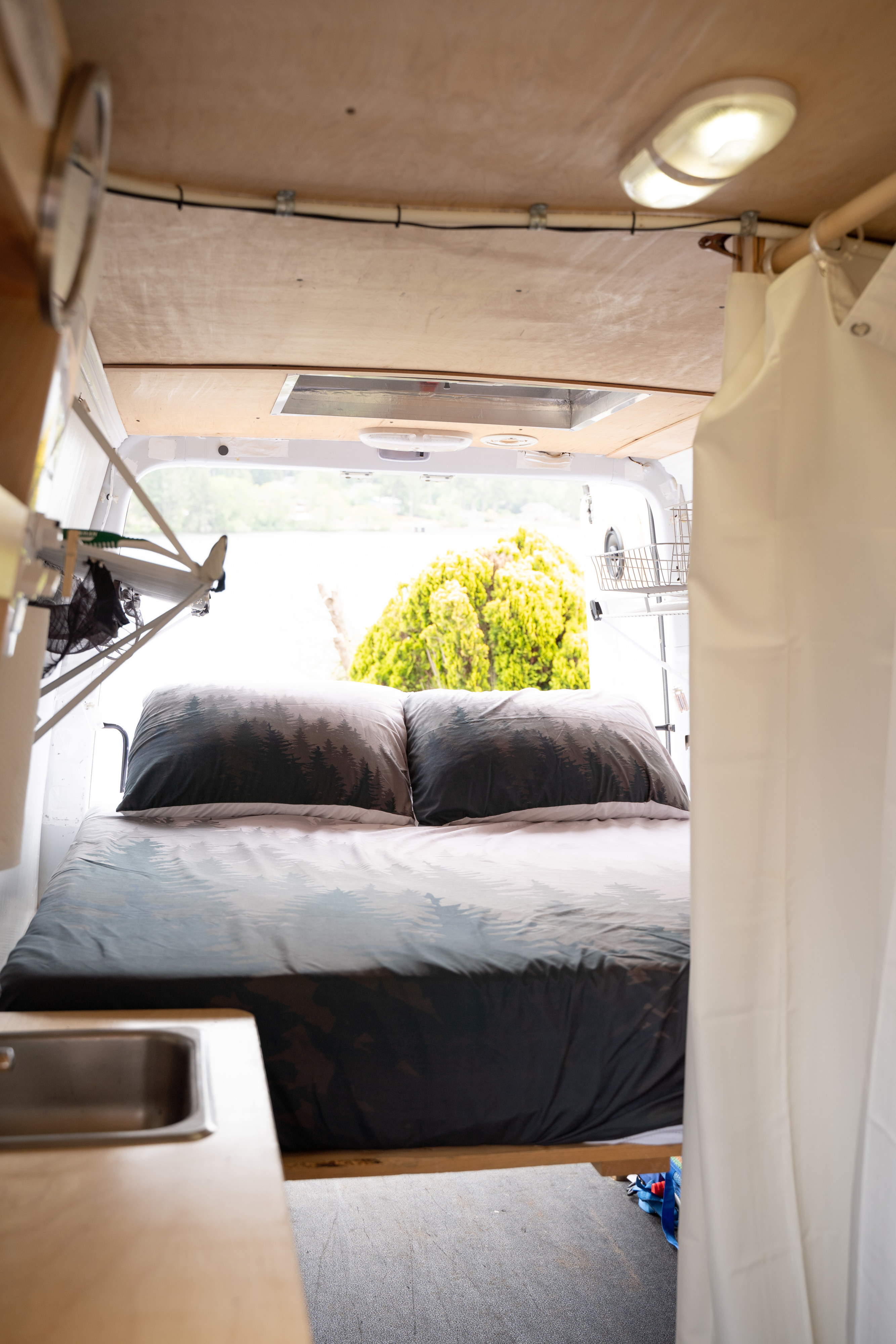 Cozy RV rental interior: a bed with forest bedding, small sink, and open back doors offering a bright lake view.. Mercedes-Benz Sprinter 2017