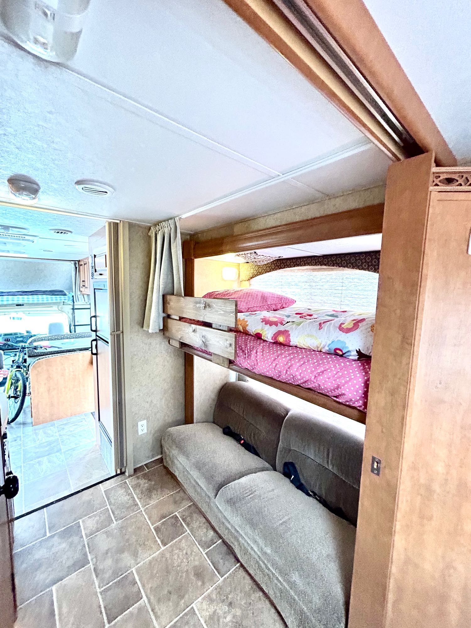 This RV rental's interior shows bunk beds (pink/floral bedding), sofa, and tile floor, with bike visible in front. Great for families!. Forest River Sunseeker 2011