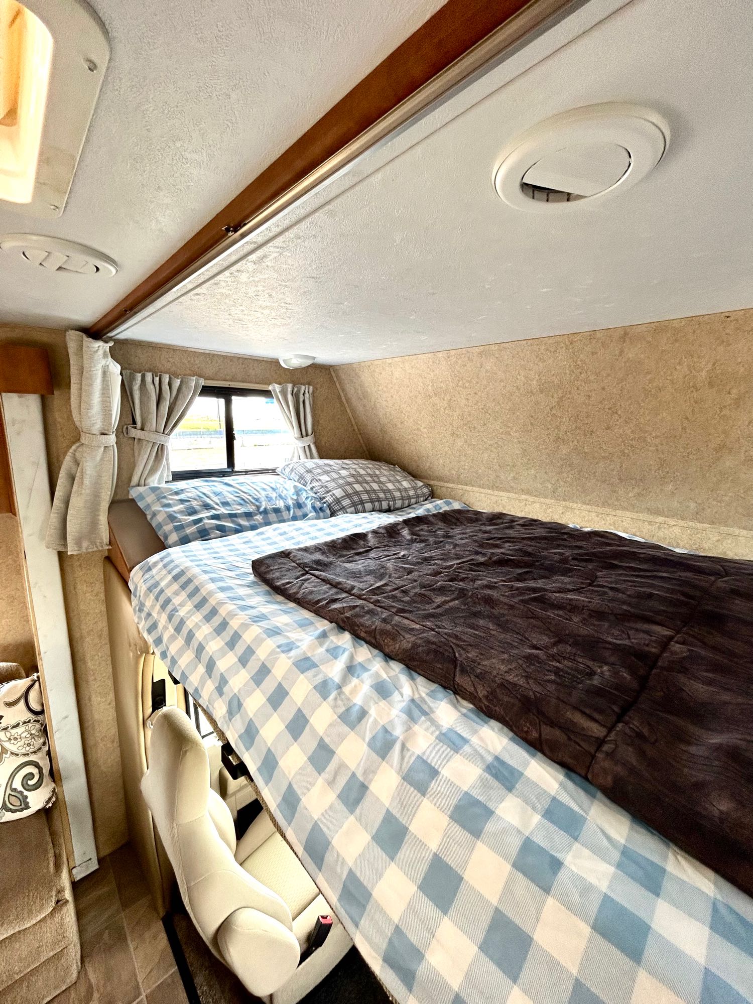 RV rental interior: a snug over-cab sleeping area with blue/white plaid bedding, brown comforter, and windows.. Forest River Sunseeker 2011