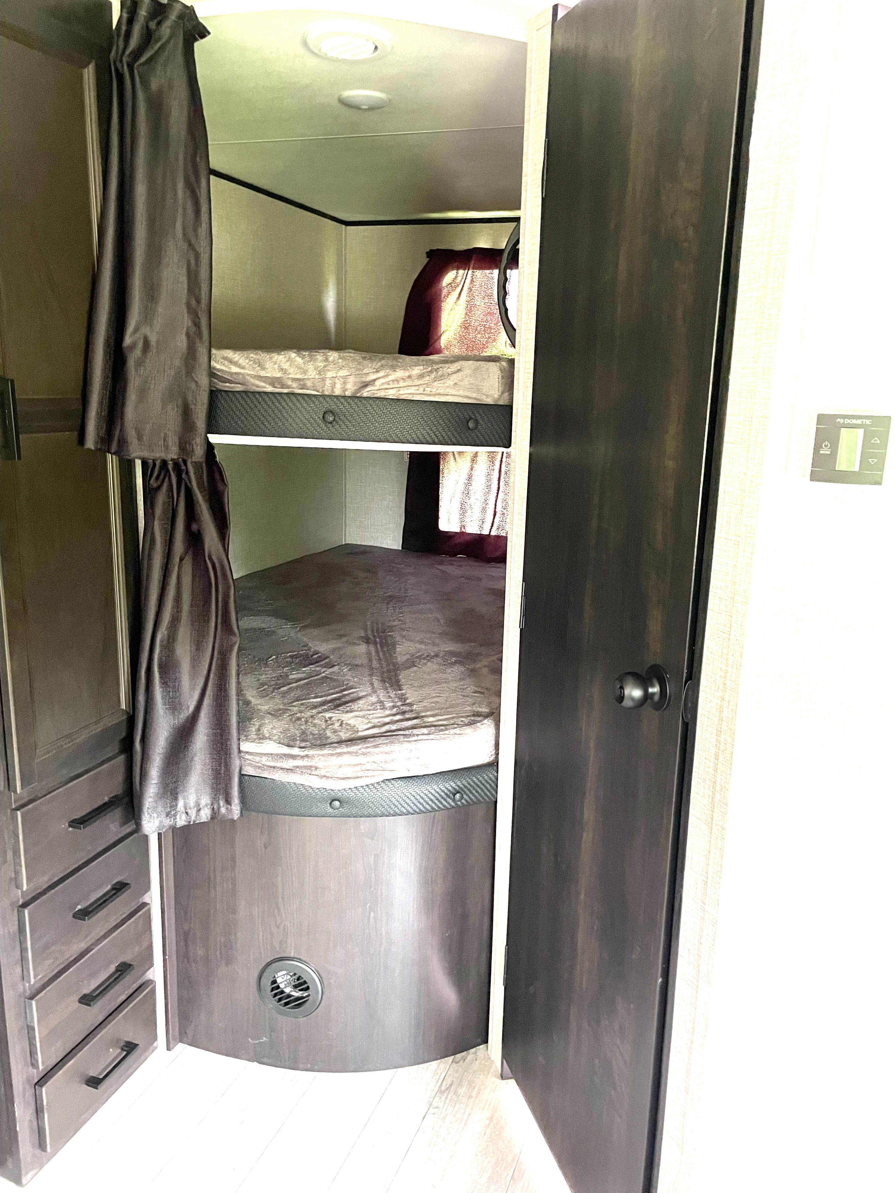This RV rental features a compact sleeping area with two stacked bunk beds, privacy curtains, and a built-in storage cabinet.. Jayco Jay Flight 2023