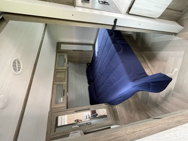 Inside an RV rental: a modern bedroom features a blue comforter, wood cabinets, and herringbone flooring. Ready for your adventure.. Forest River Wildwood Heritage Glen HL 2022