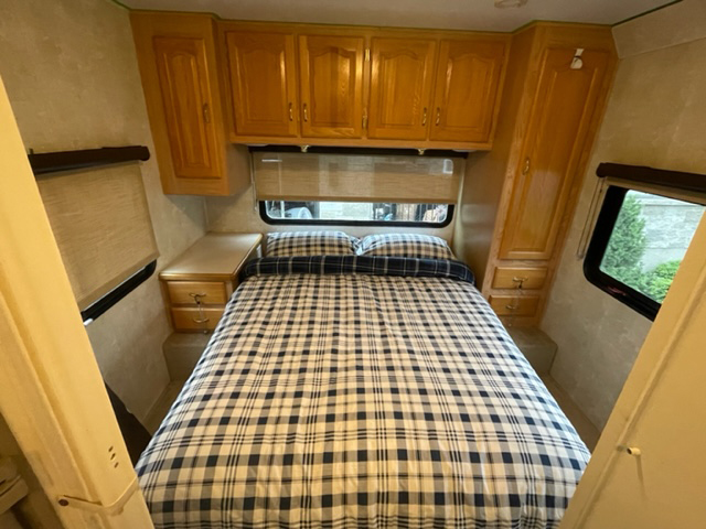 Cozy RV rental bedroom with a plaid bed, overhead wood cabinets, and window blinds. Perfect for comfortable travel.. FORD SUNSEEKER 2004