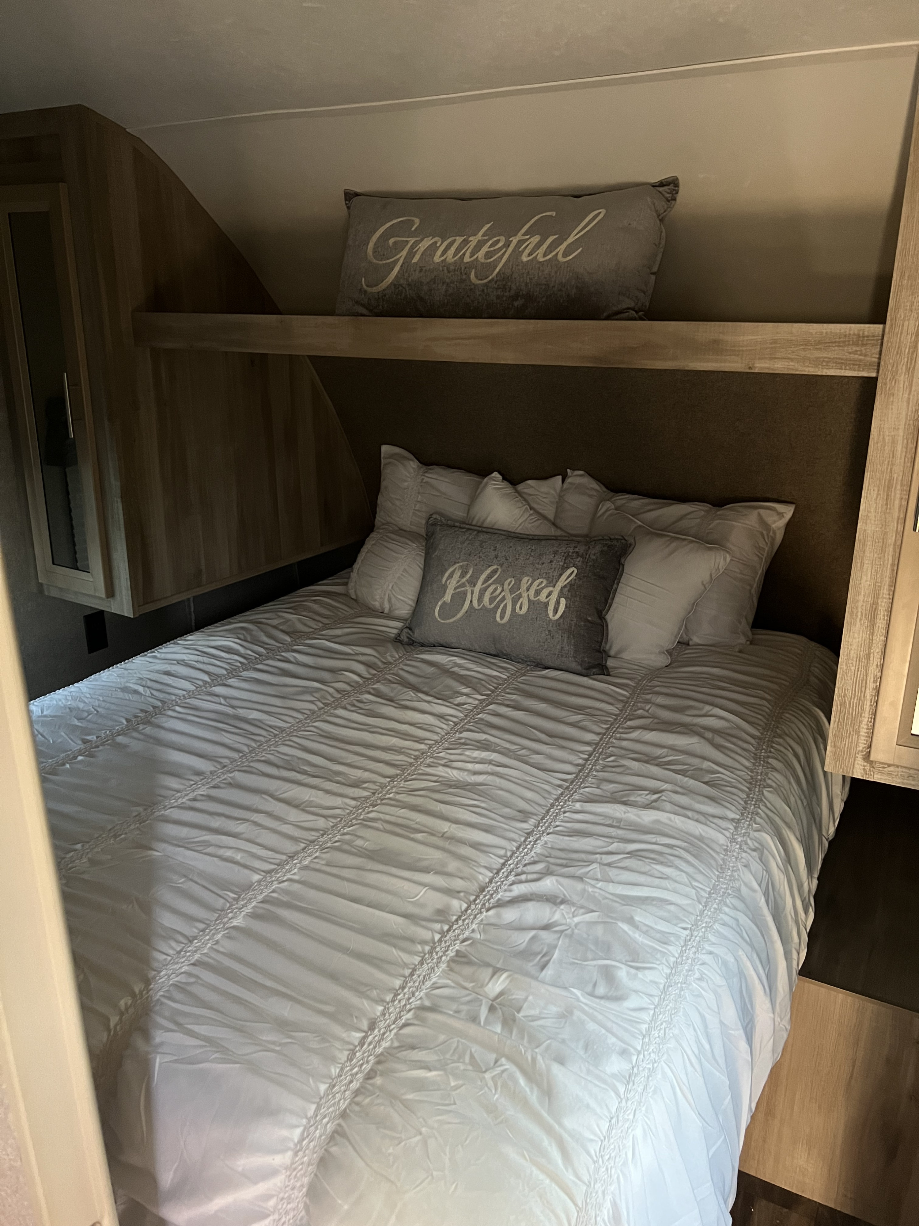 A cozy and clean RV rental bedroom, featuring a neatly made bed with white ruffled bedding and "Blessed" and "Grateful" pillows.. Forest River Coachmen Catalina SBX 2019