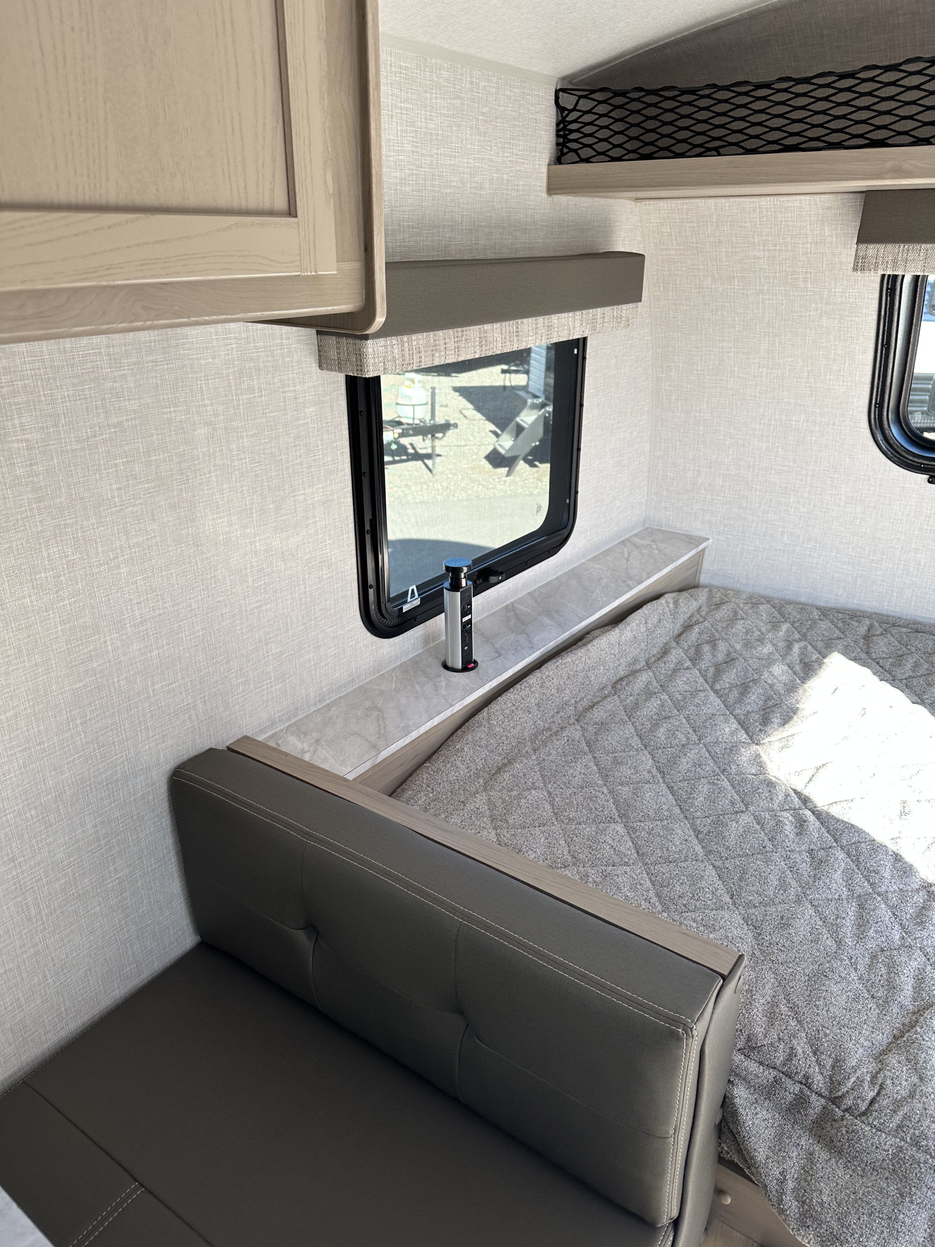 RV rental interior: Bright bedroom with gray bed, dark gray seating, & pop-up outlet.. Forest River Flagstaff E-Pro 2023