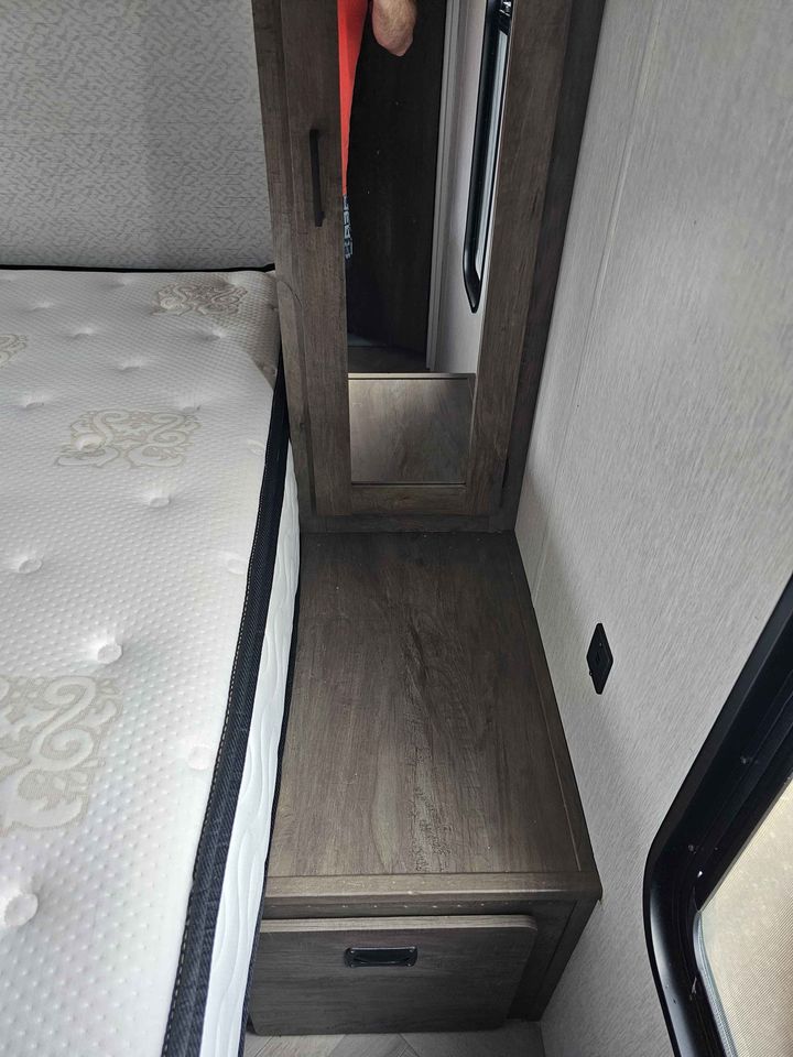 RV rental bedroom: comfy mattress, wooden mirrored cabinet, nightstand with drawer storage, and window.. Forest River Salem Cruise Lite 2022