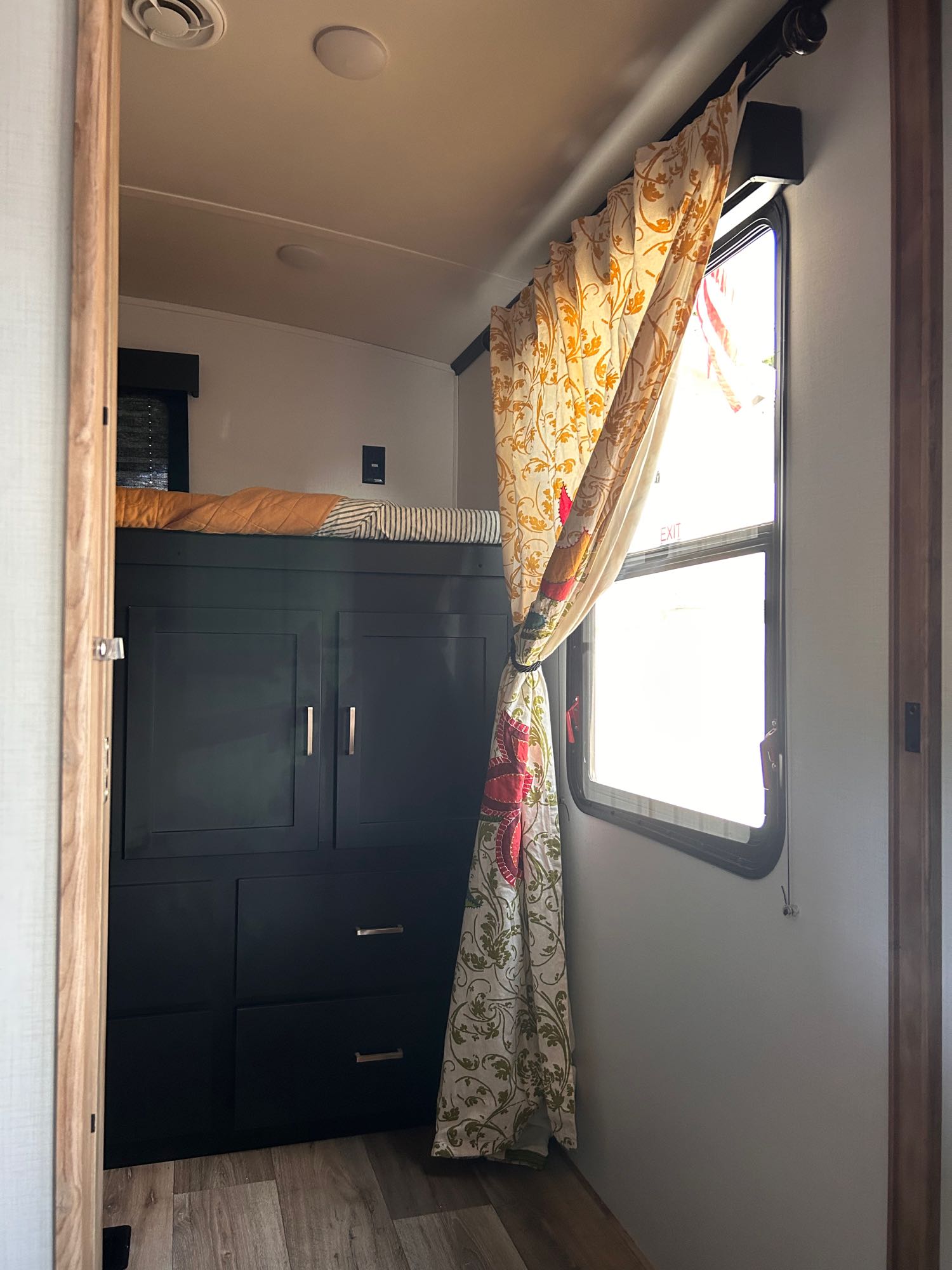 Cozy RV rental interior showing bunk beds, black storage cabinets, and colorful tied-back curtains by a window.. Keystone RV Outback Ultra-Lite 2022