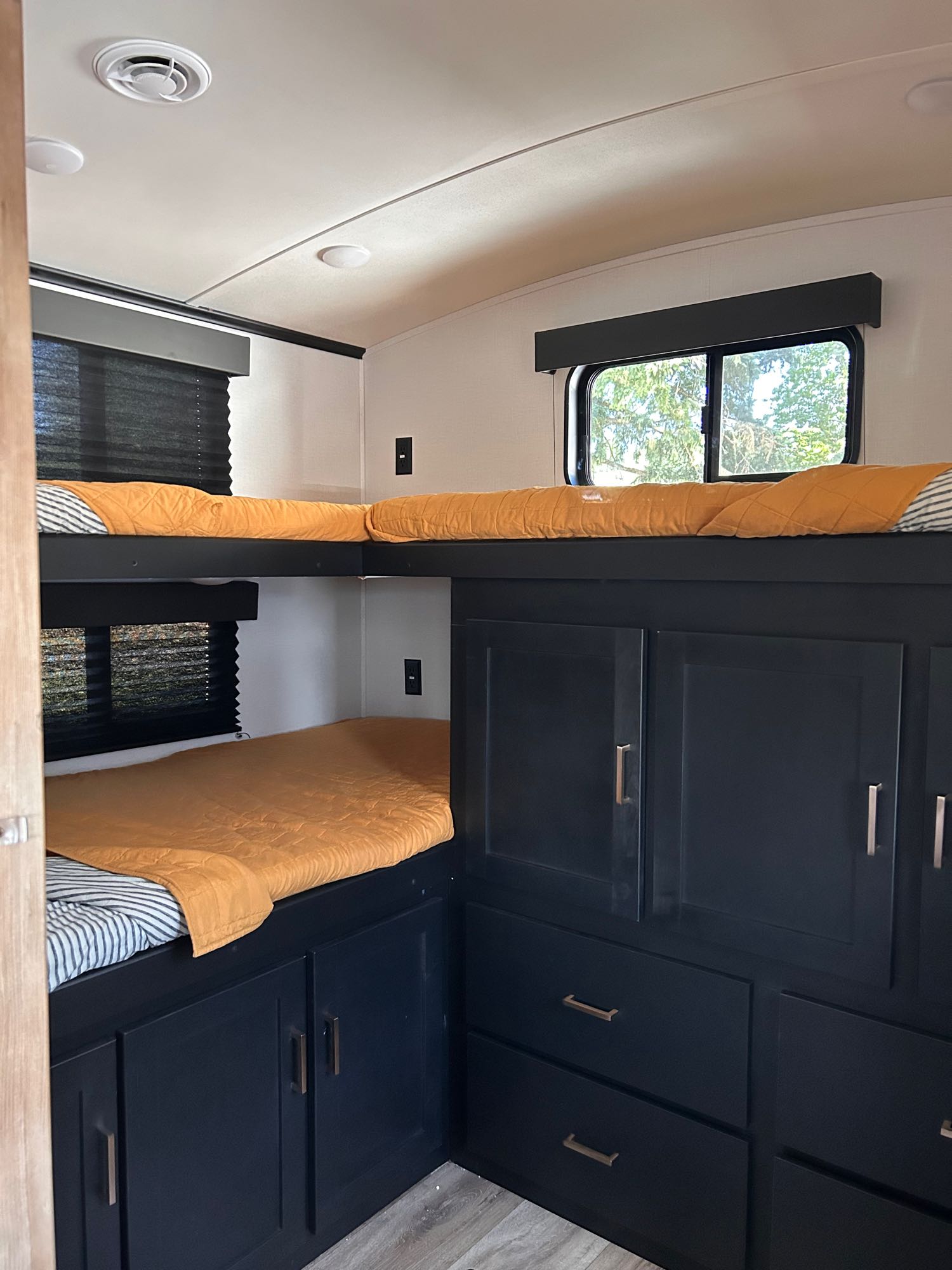 Inside an RV rental: a modern bunkhouse with comfy bedding, windows, & dark blue storage cabinets for travel.. Keystone RV Outback Ultra-Lite 2022
