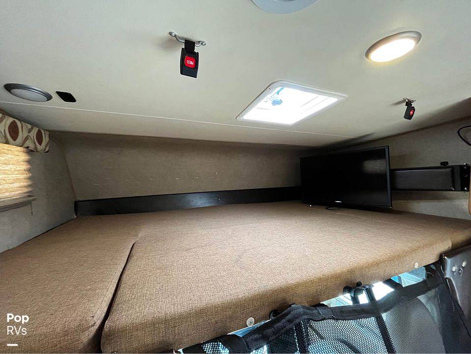 Spacious RV rental overhead bed area with a TV, skylight, and safety straps for a comfortable stay.. Coachmen Leprechaun 2015