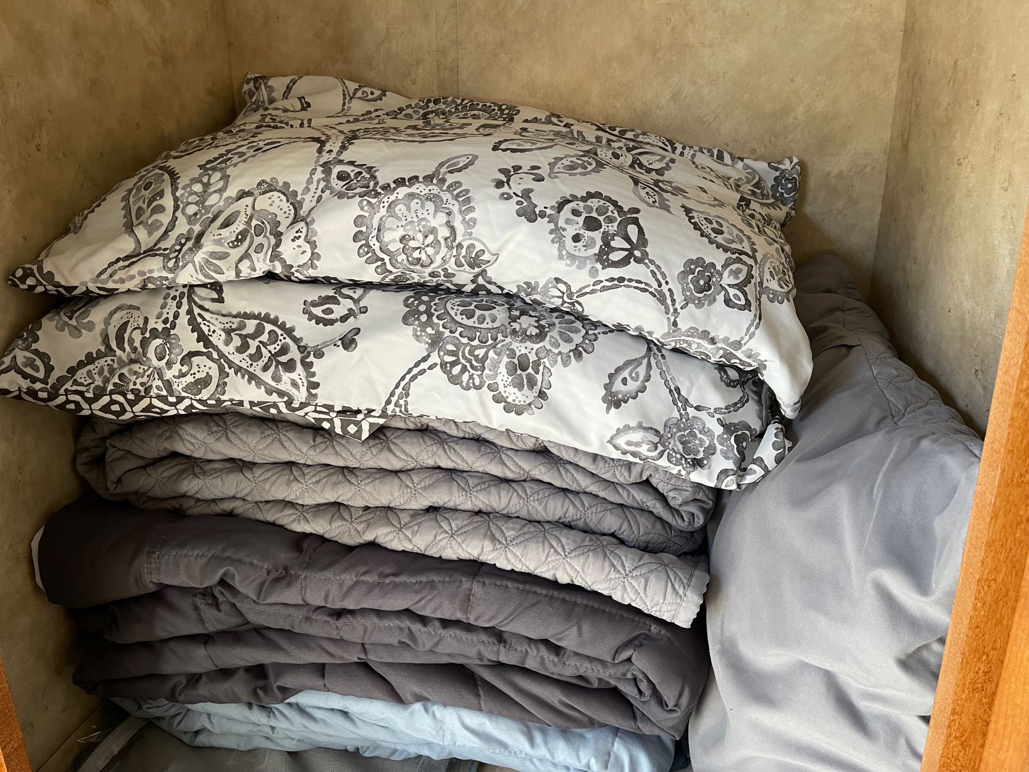 RV rental storage: Neatly stacked bedding in a cupboard – patterned pillows, grey quilts, and blankets for a cozy stay.. GULF W6211 2008