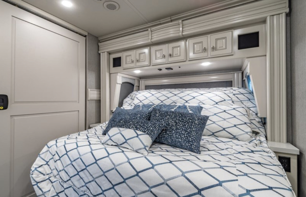 Cozy RV rental bedroom with patterned bed, overhead cabinets, and modern design. Ideal for comfortable travel accommodations.. Fleetwood Discovery LXE 2023