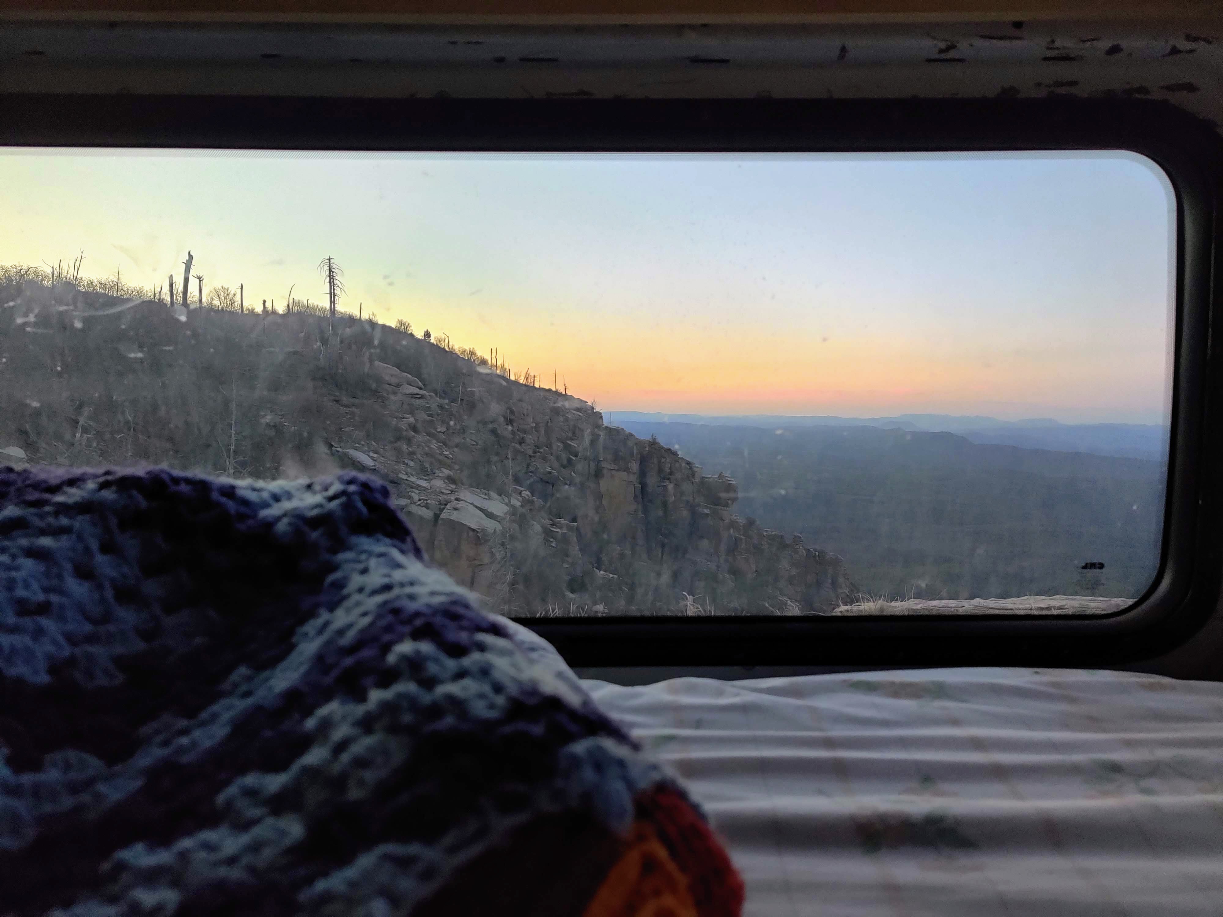 Cozy RV rental view: stunning sunset over rugged mountains, seen from a comfy bed, offering a serene landscape.. Nissan Other 2012