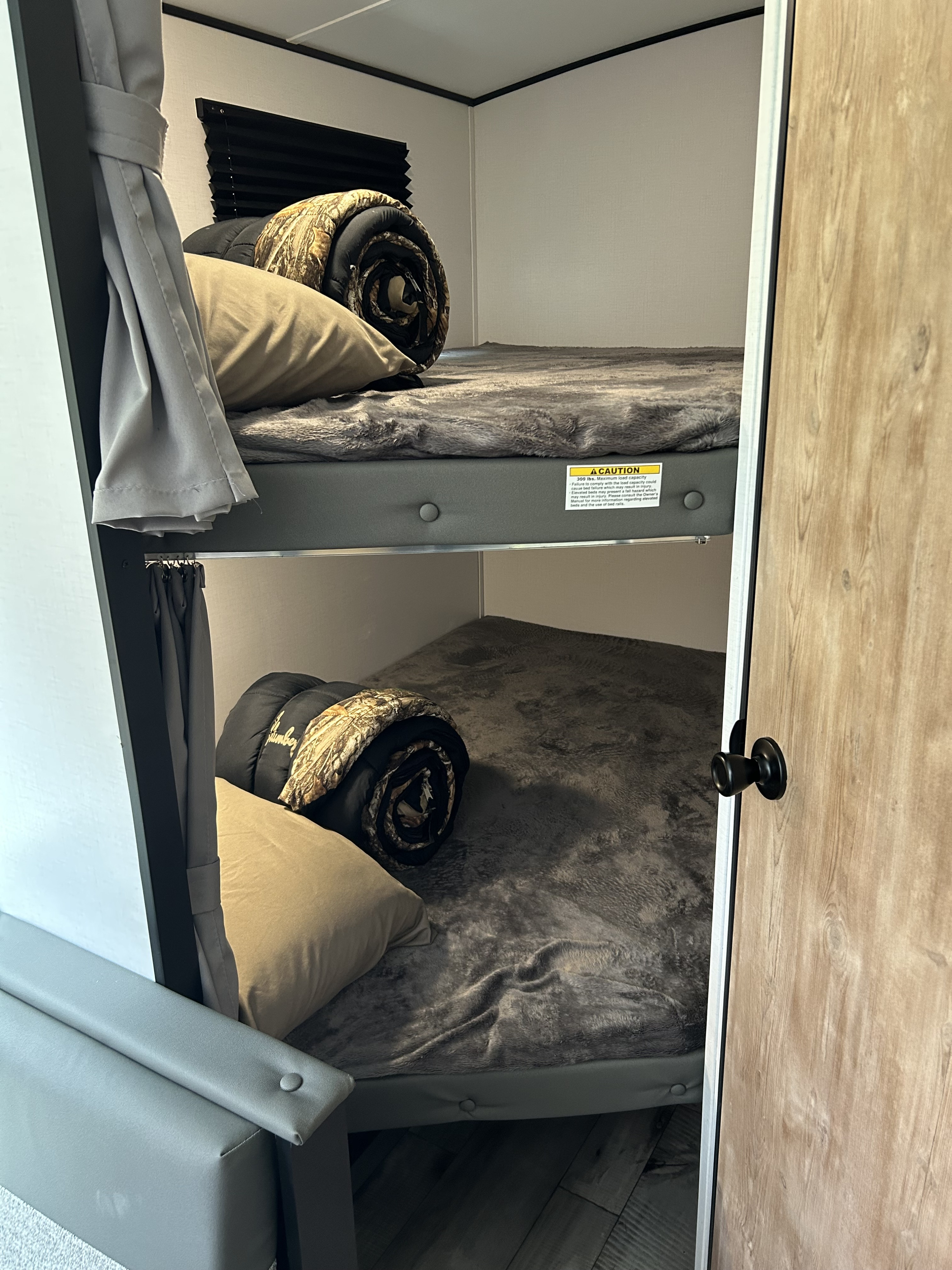 Cozy RV rental bunk beds with soft gray bedding and camouflage rolls, perfect for compact camper adventures.. Keystone RV Springdale 2022