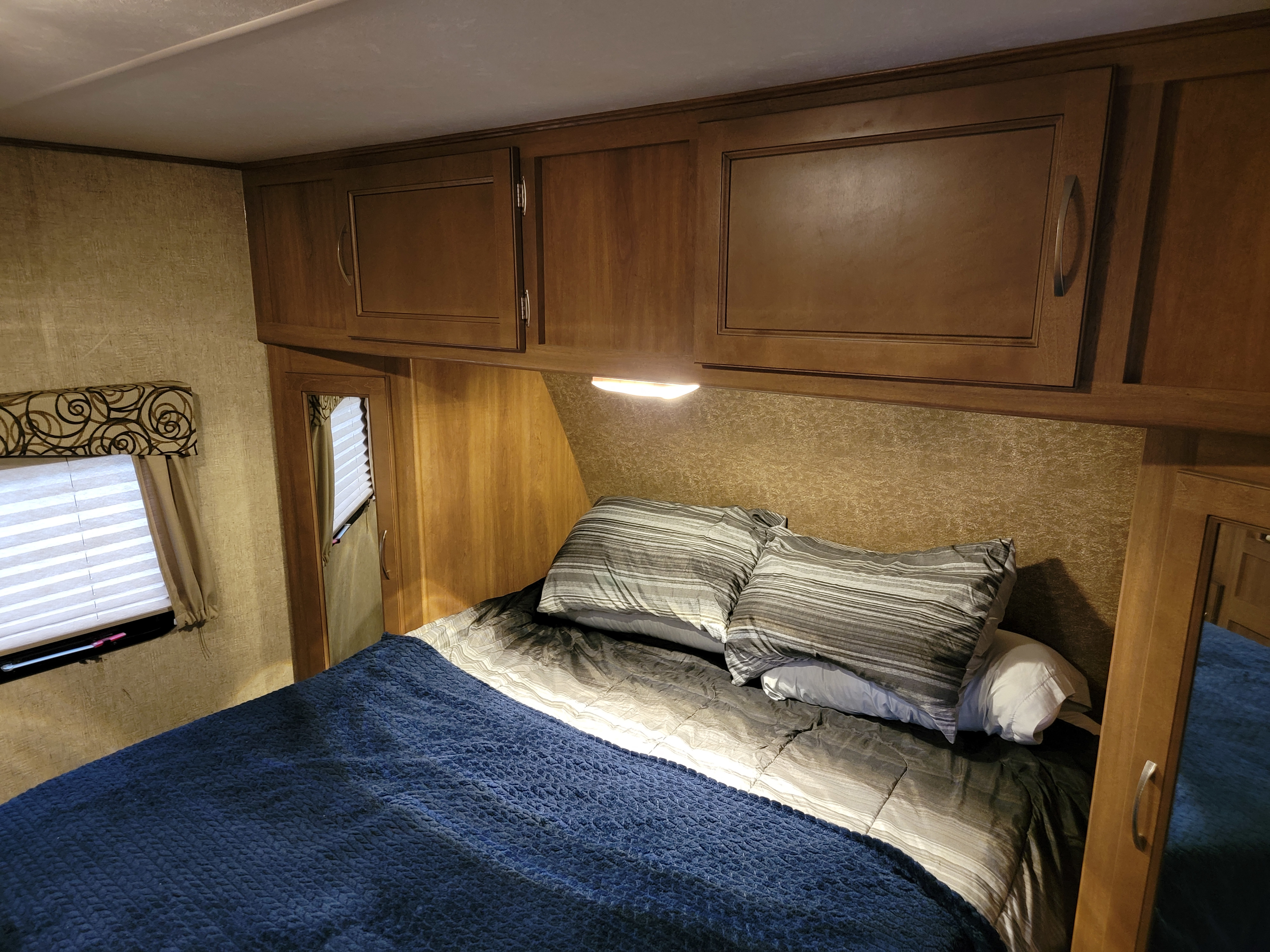 Cozy RV rental bedroom with wood cabinets, comfy bed, and window, offering a compact, inviting interior space.. Coachmen Apex 2015