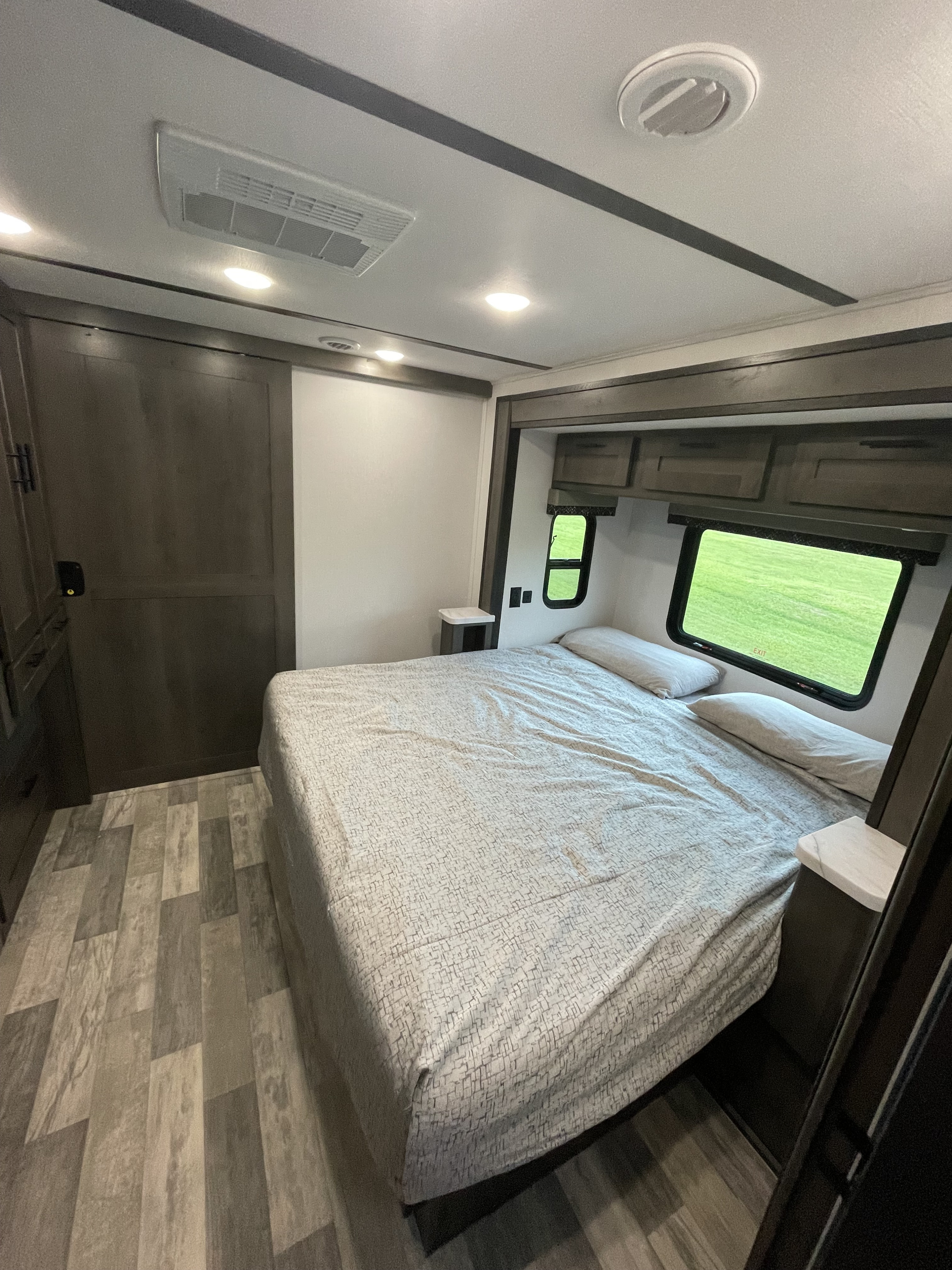RV rental bedroom: a modern space with a large bed, patterned comforter, windows showing green landscape, and wood-look flooring.. FR3 FR3 Motorhome 2023
