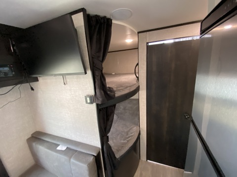 This RV rental offers a compact living area with TV, bench seating, and curtained bunk beds. A door leads elsewhere.. Jayco Jay Flight SLX 2022