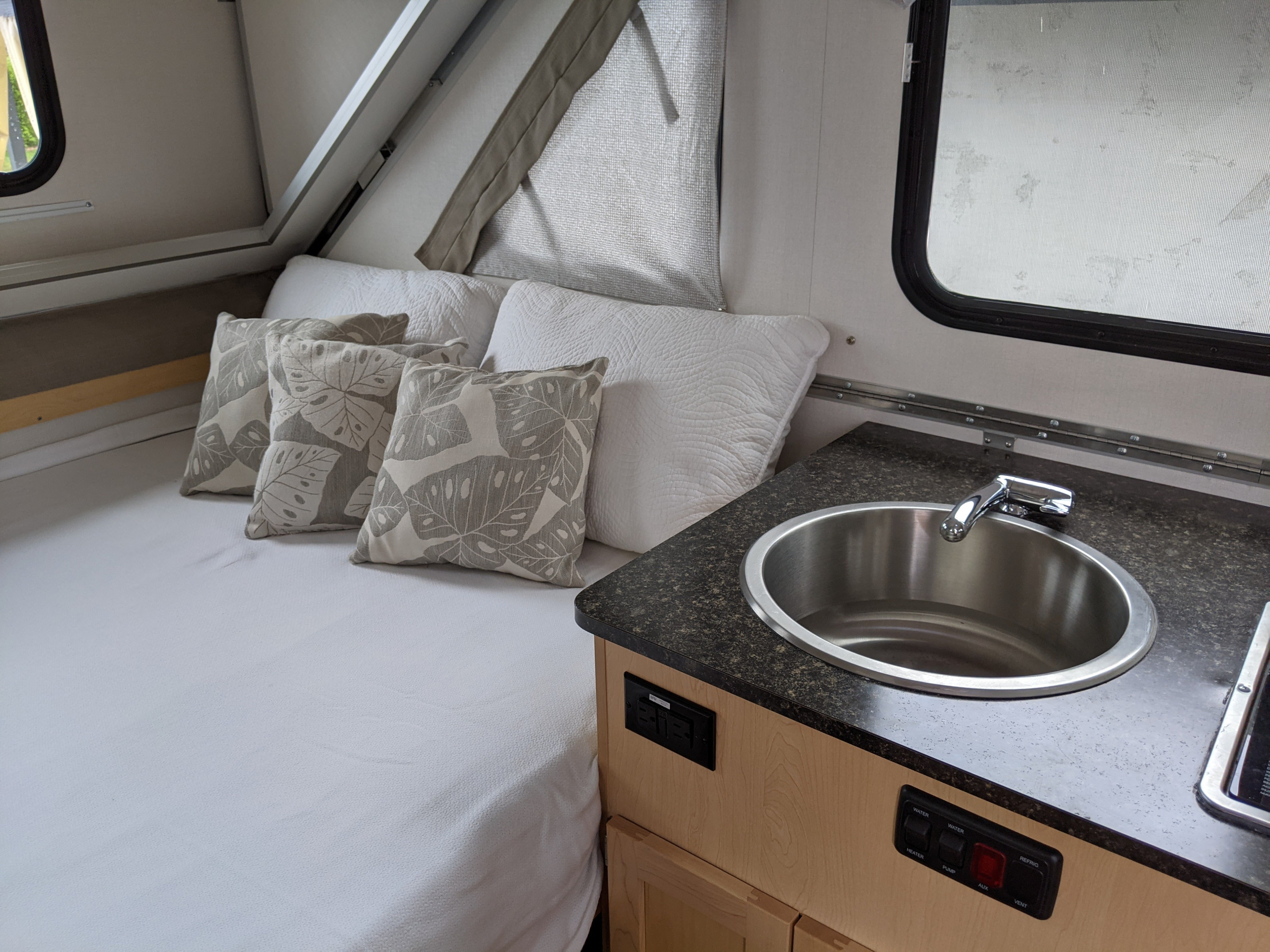 A-frame RV rental interior with a made-up bed, decorative pillows, and compact kitchen featuring a sink.. A Liner Expedition 2022