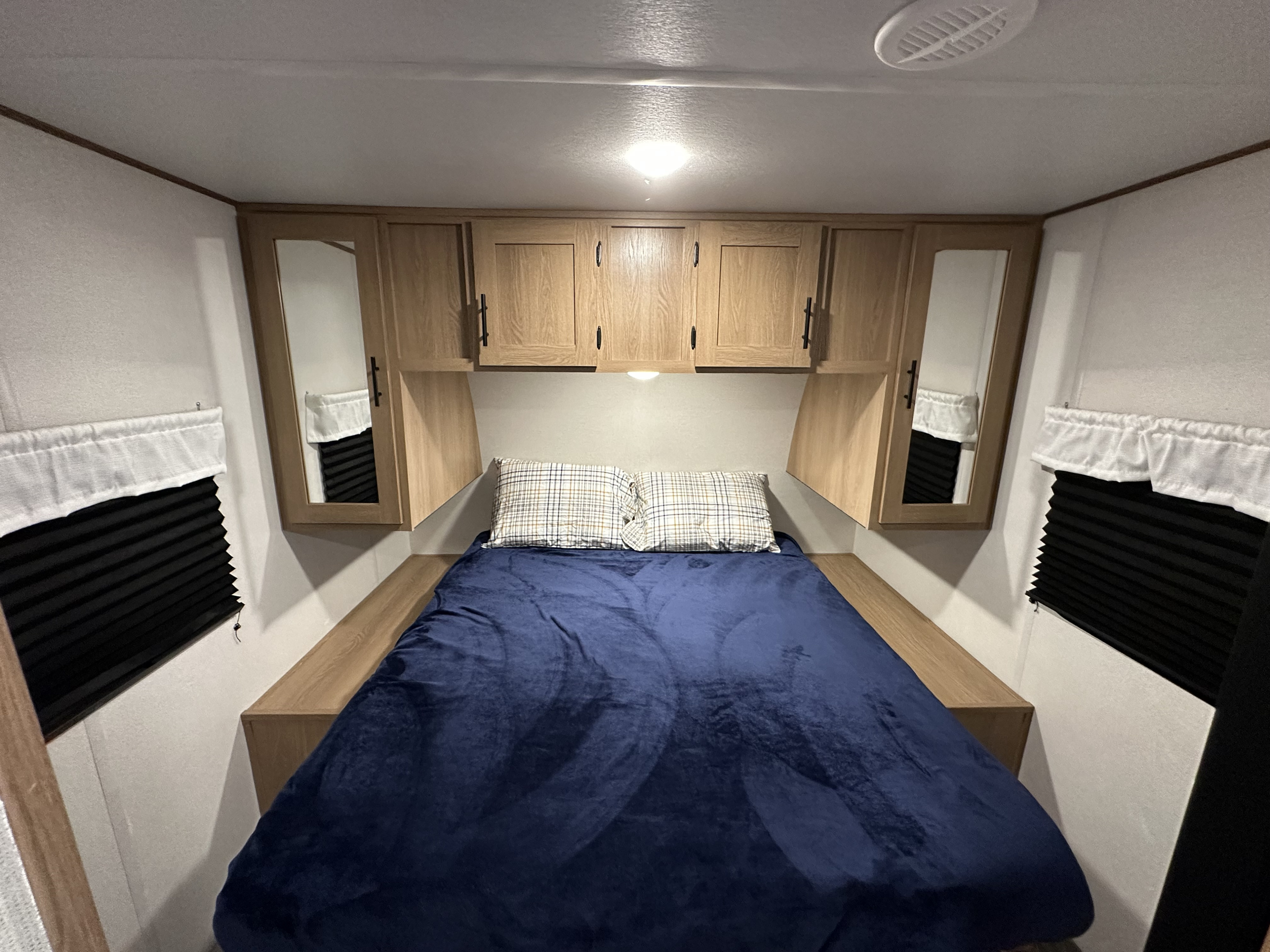Cozy RV rental bedroom with a comfy bed, blue blanket, pillows, light wood cabinets, and window blinds.. Prime Time RV Avenger 2022