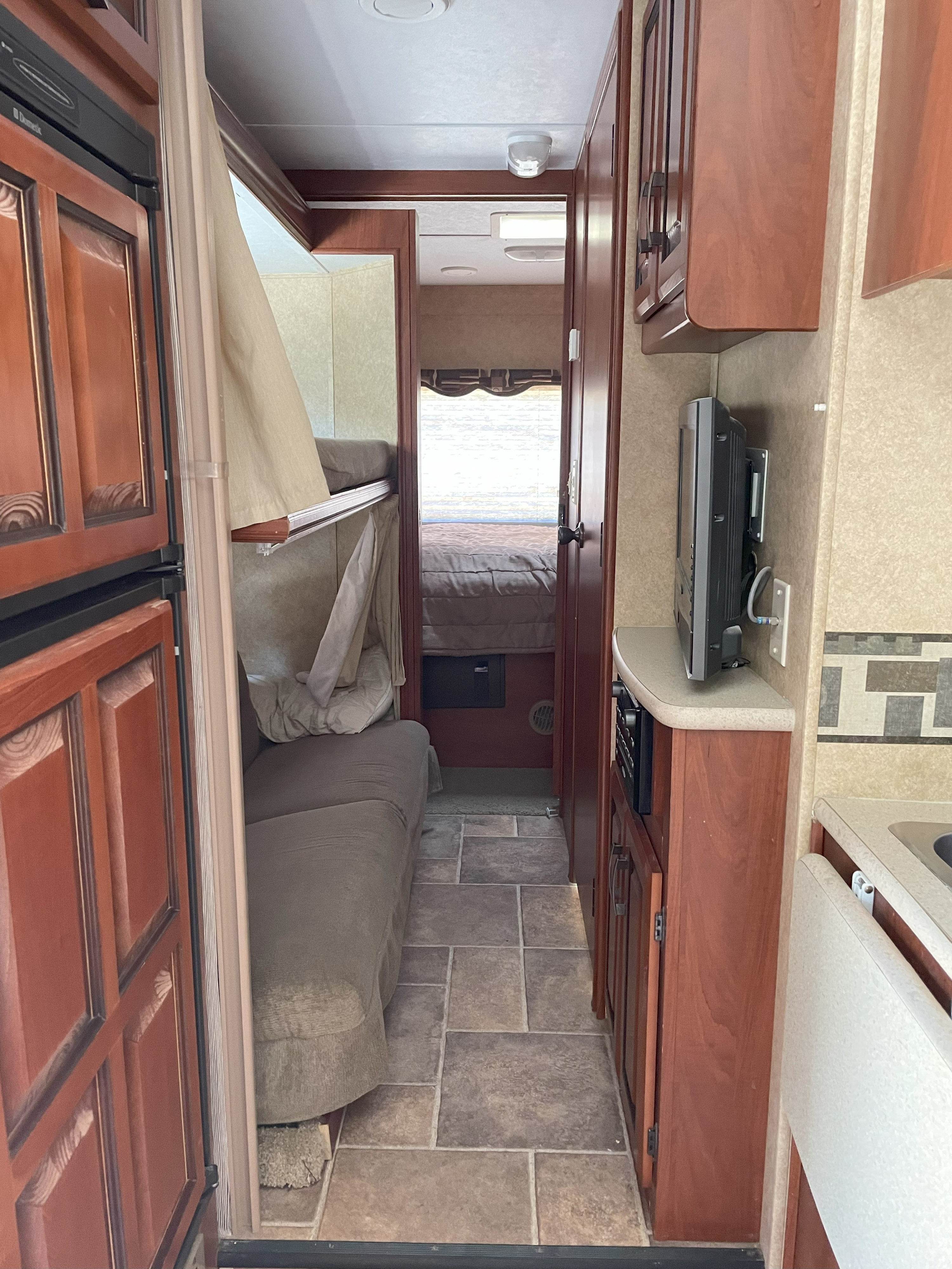 RV rental interior: a hallway view with a refrigerator, bunk beds, kitchen counter, TV, and private bedroom beyond.. Forest River Sunseeker 2011
