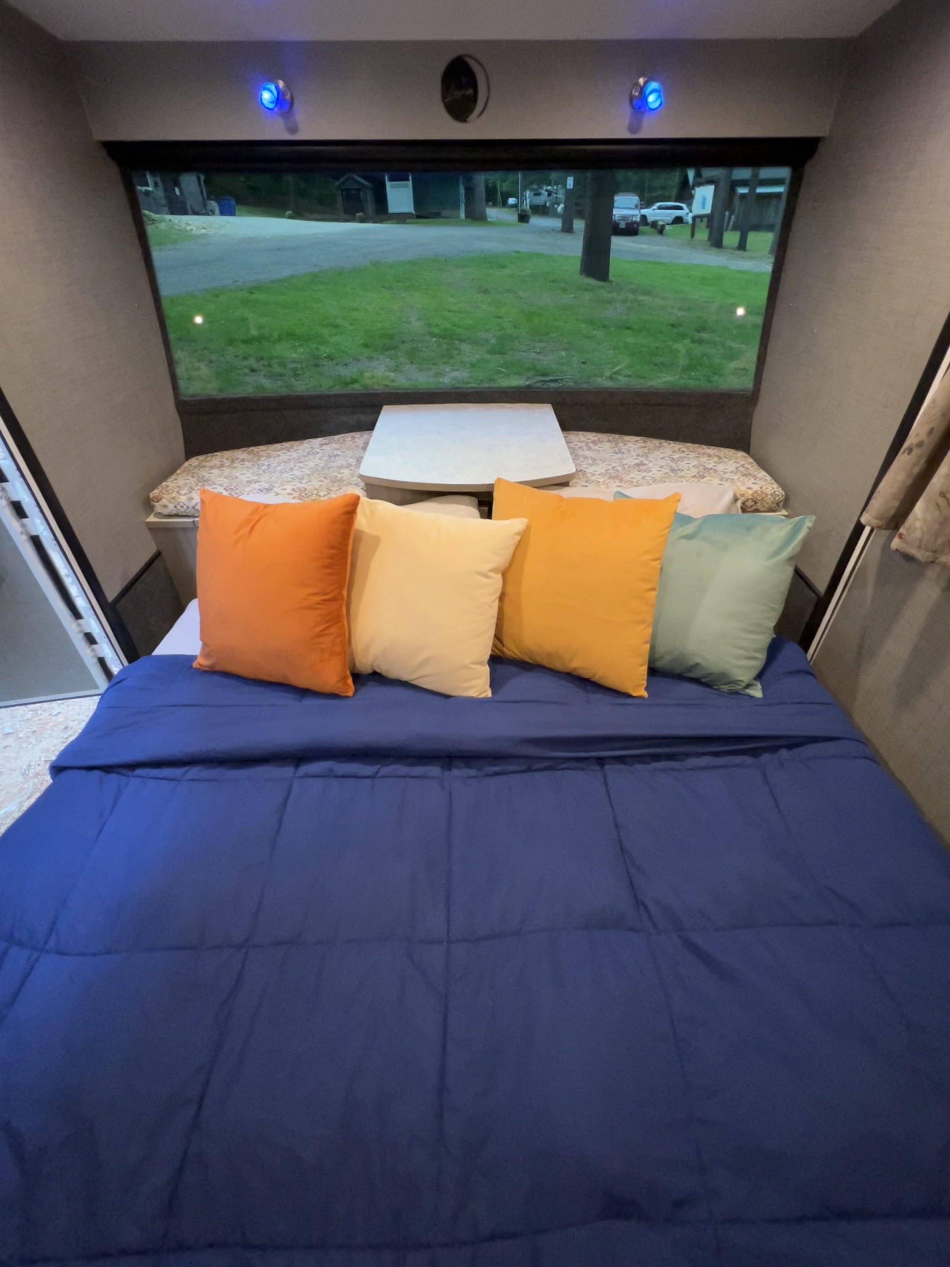 Cozy RV rental interior with a blue comforter, colorful pillows, and a large window view of a campsite.. InTech RV InTech RV Trailer 2018