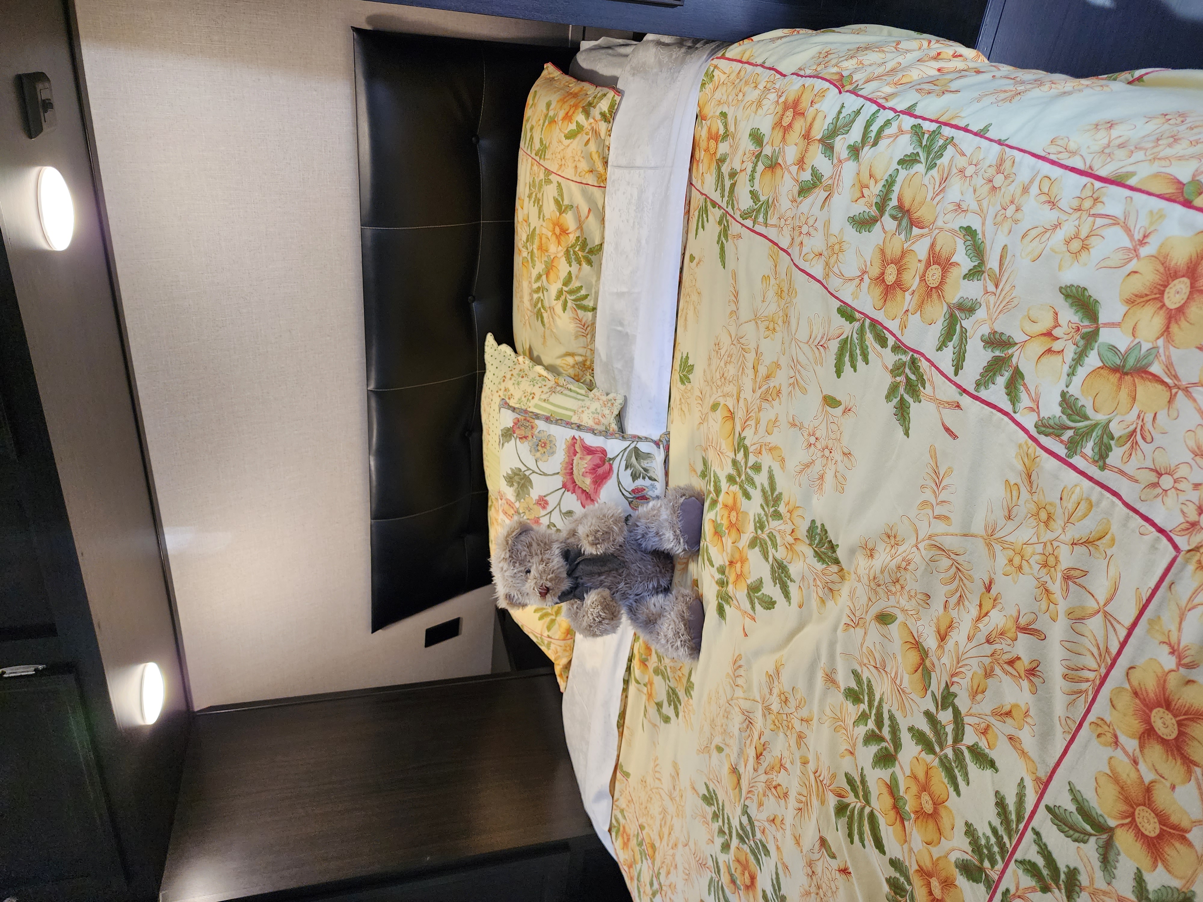 RV rental bedroom: a bed with vibrant floral bedding, dark headboard, and a plush teddy bear, offering a cozy retreat.. Venture Sporttrek 2018