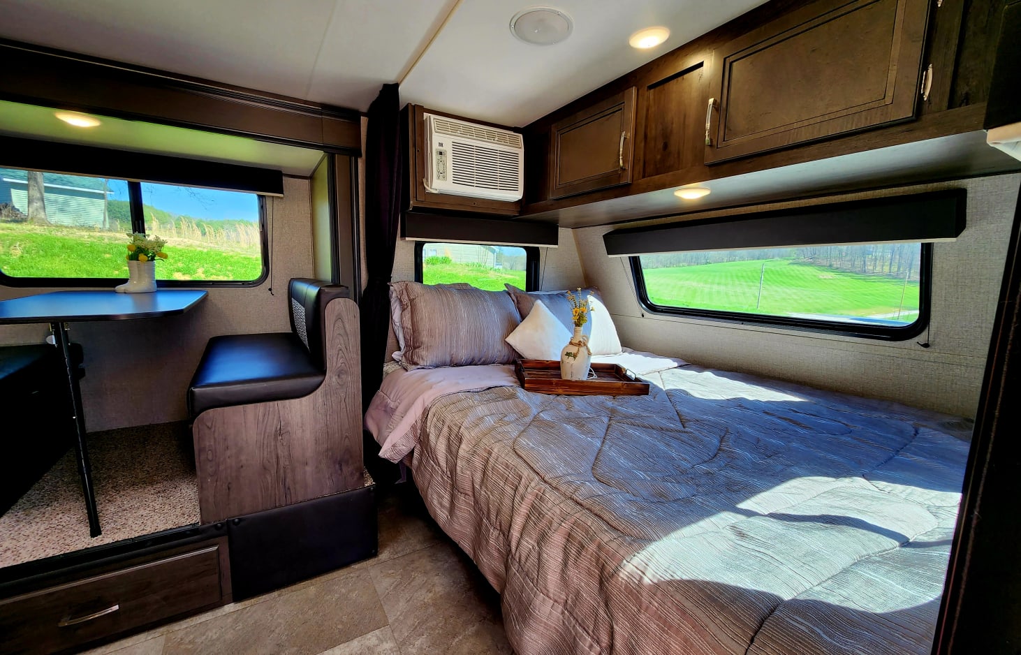 Interior of a modern RV rental: a comfy bed, dinette, and large windows framing lush green outdoor scenery.. Jayco Jay Flight SLX 2020