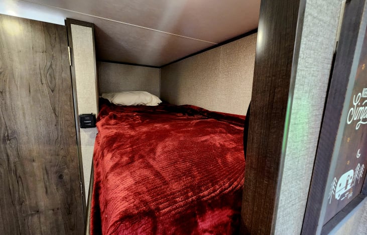 Inside an RV rental: a compact, cozy bunk bed with a soft red blanket and white pillow, perfect for rest on the road.. Jayco Jay Flight SLX 2020