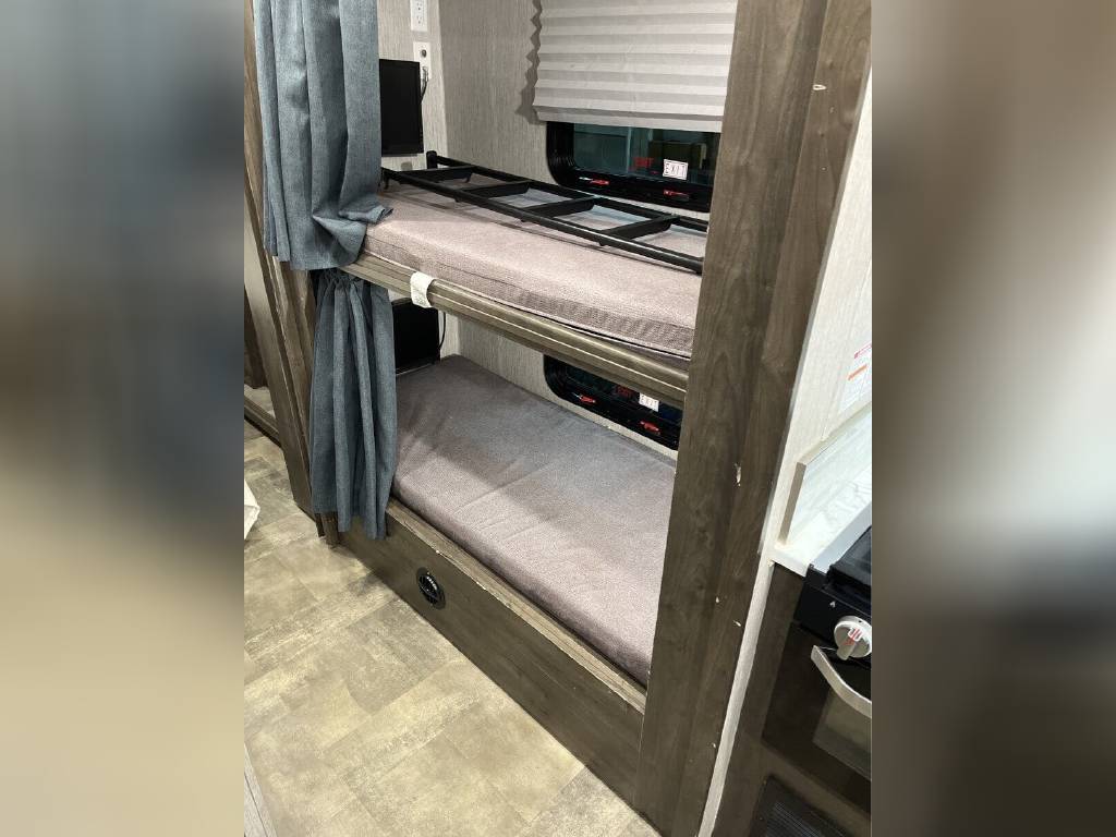 This RV rental features cozy bunk beds with privacy curtains and a compact kitchen area, ideal for family travel.. Forest River Coachmen Pursuit 2022