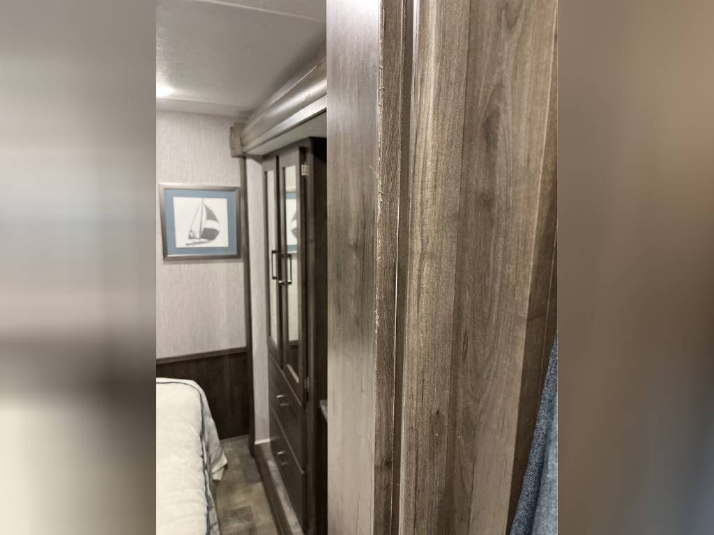 RV rental interior: A compact bedroom with a bed, framed sailboat art, and a mirrored wardrobe. Features modern wood-look finishes.. Forest River Coachmen Pursuit 2022