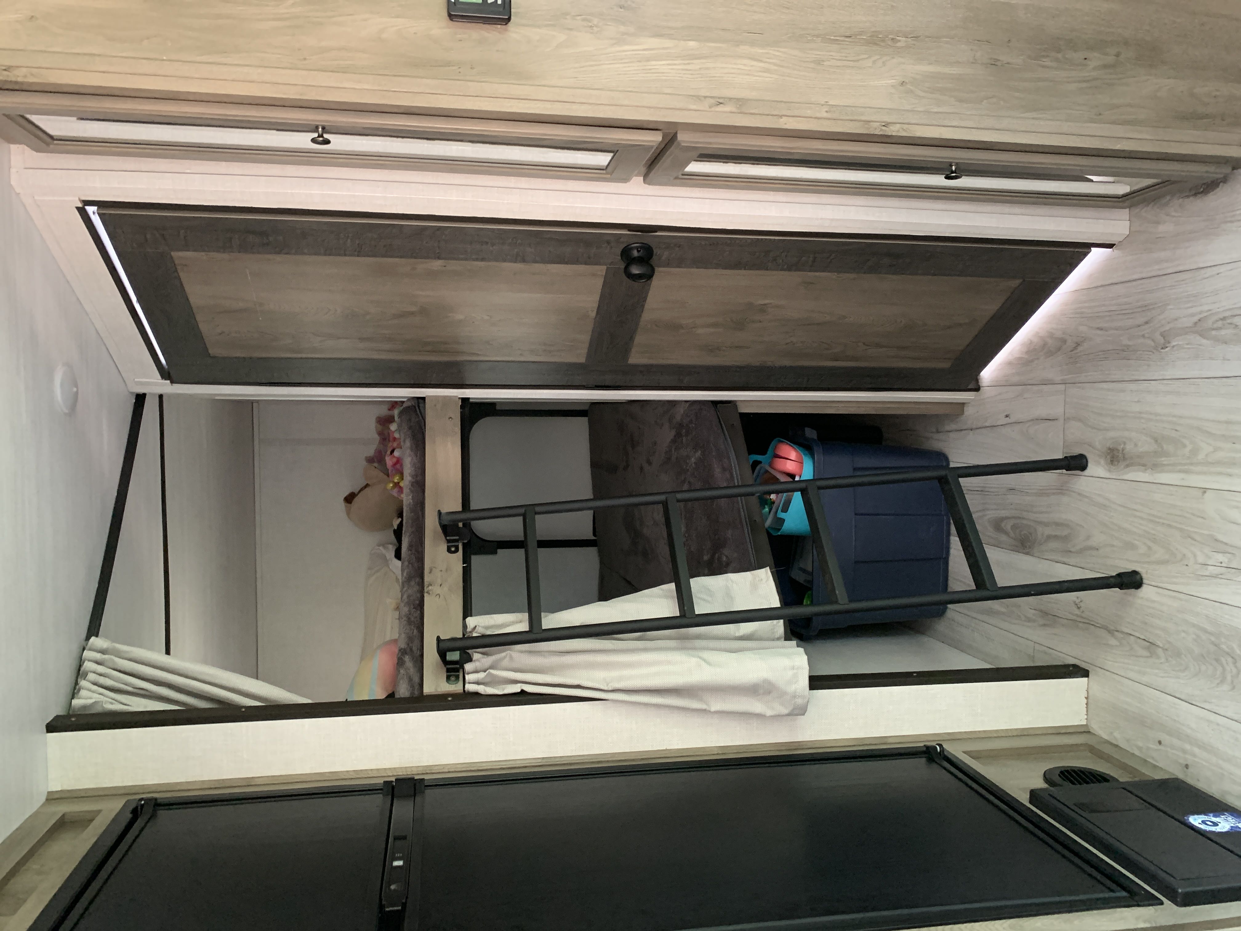 RV rental bunk beds with a ladder, overhead storage cabinets, and light-colored interior finishes.. Forest River Surveyor Legend 2022