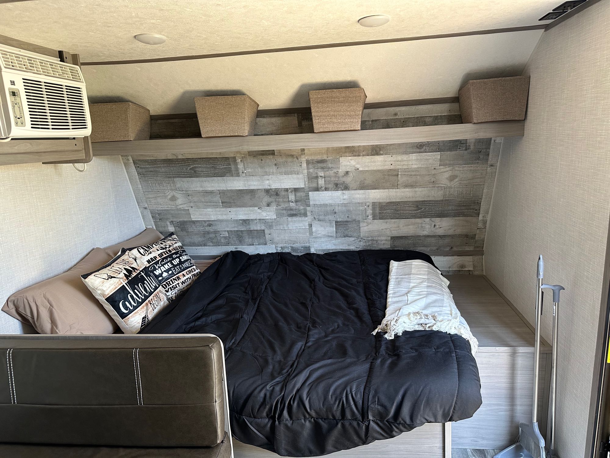 Cozy RV rental bedroom featuring a bed with camping pillow, overhead shelf with baskets, and AC unit.. Coleman Lantern LT 17B 2023