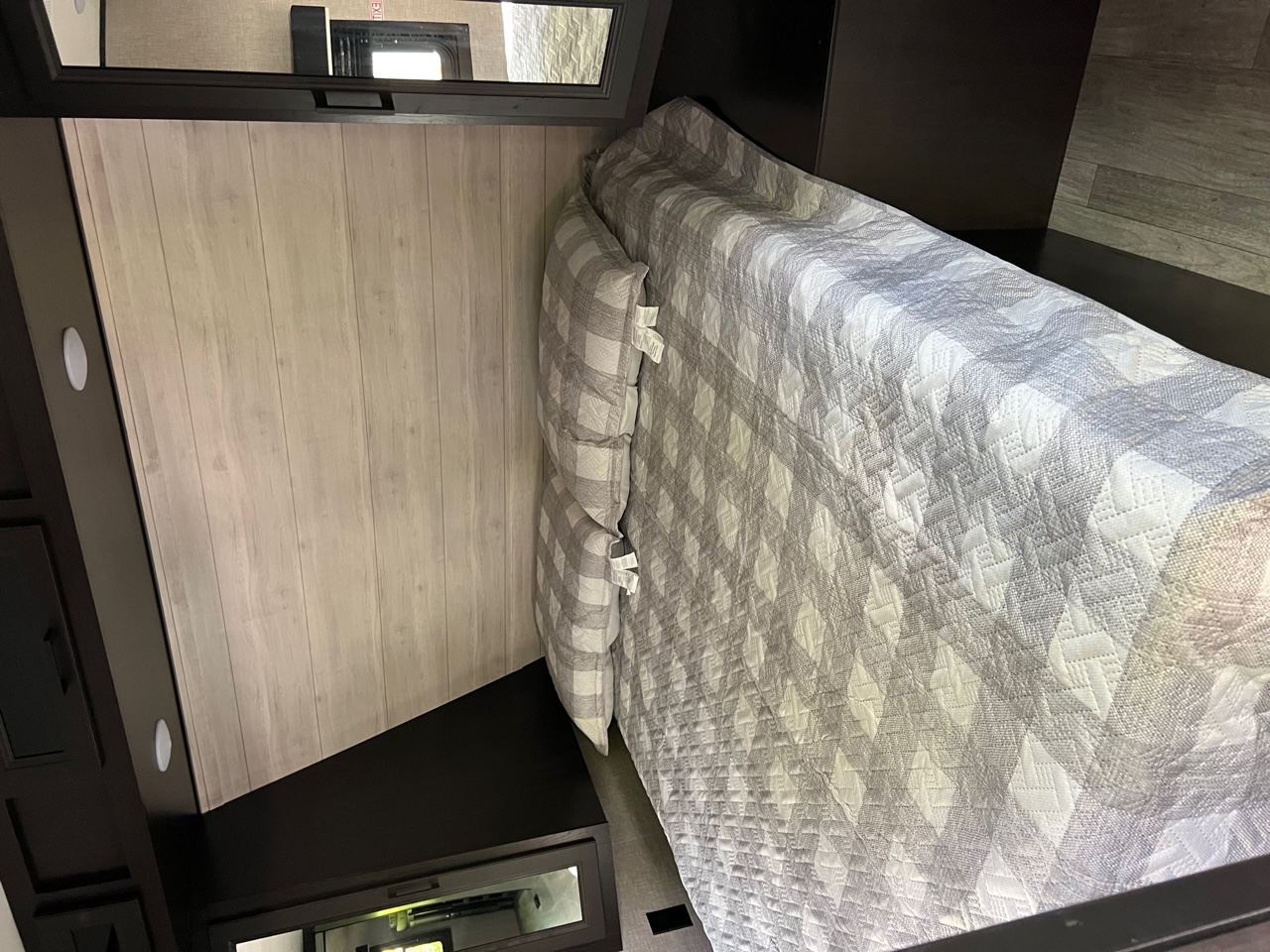 Inviting RV rental bedroom with a grey checkered comforter, light wood paneling, and dark built-in storage.. Jayco Jay Flight 2022
