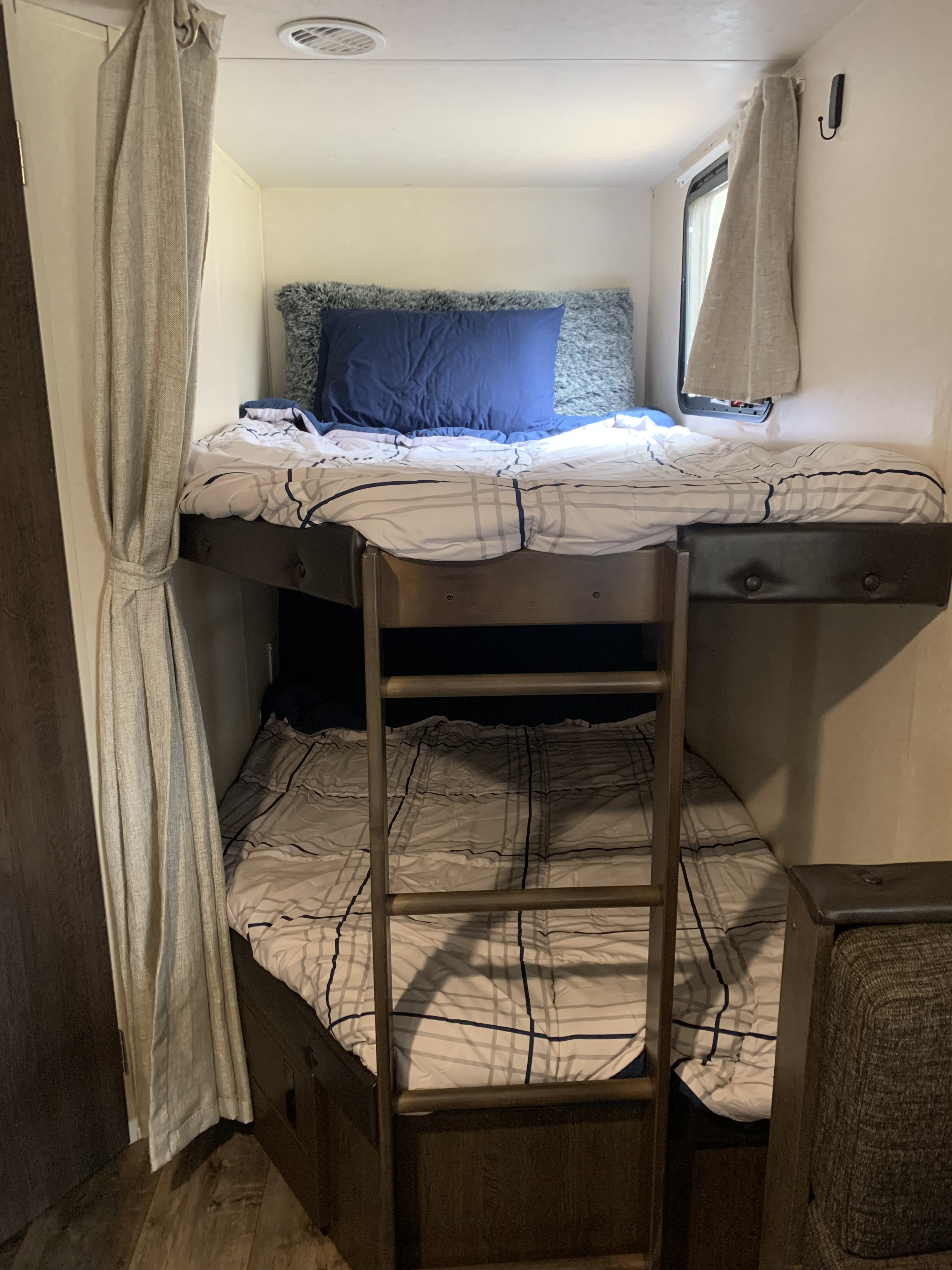RV rental showing cozy bunk beds with plaid bedding, a ladder, and beige curtains inside a well-lit compact space.. Forest River Salem Cruise Lite 2018